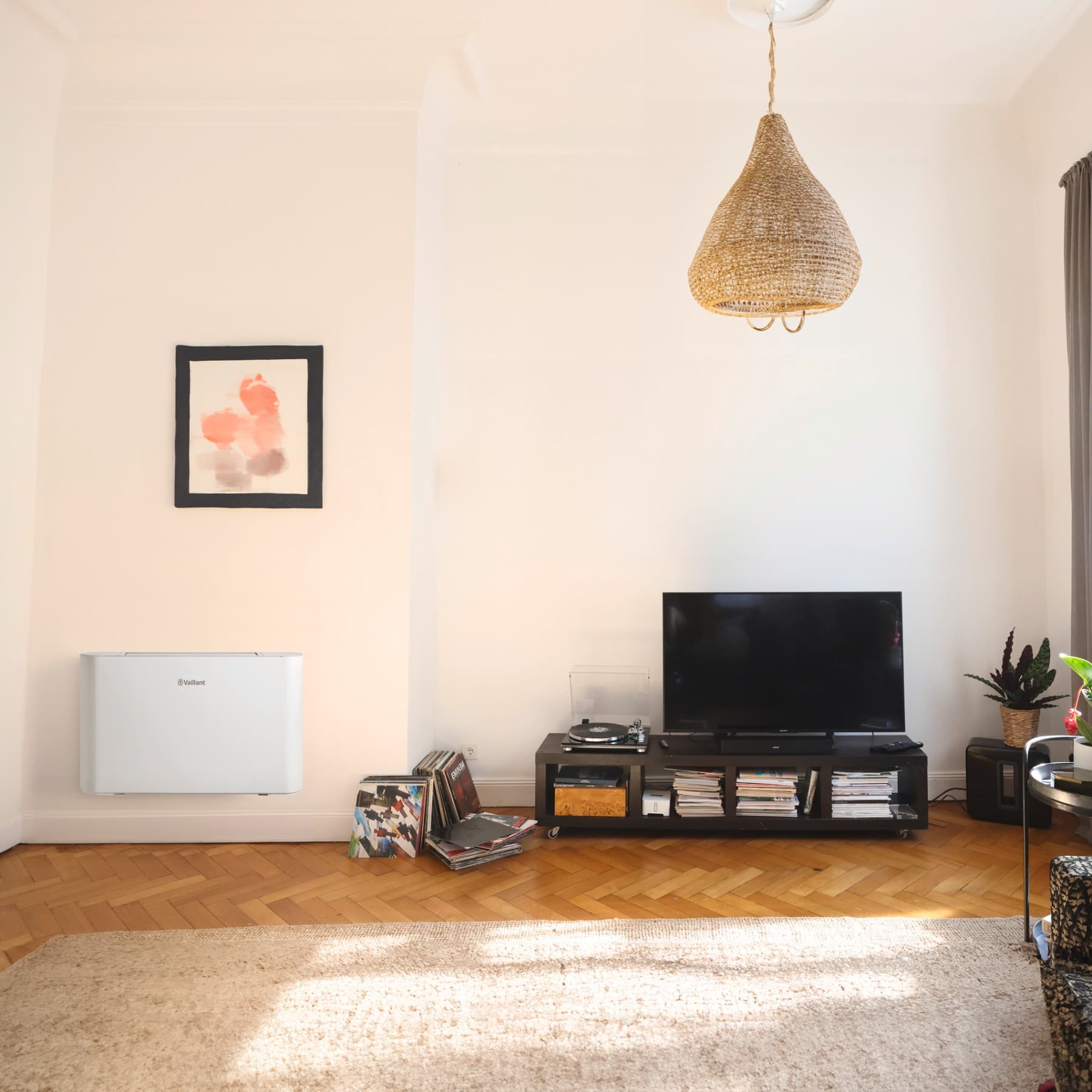 Ein Vaillant Gebläsekonvektor hängt an einer Wand im Wohnzimmer neben einen TV Board.