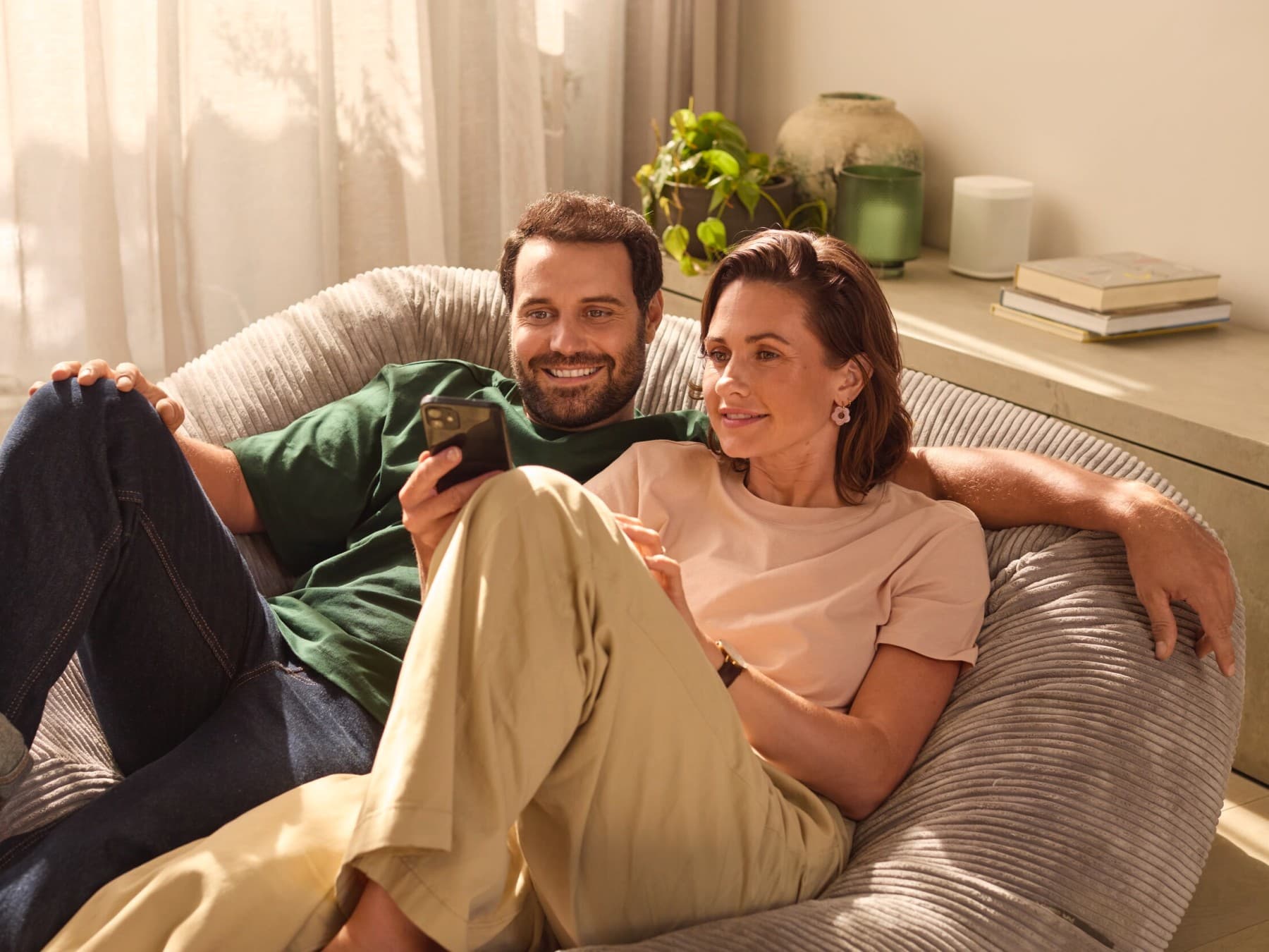 Ein Mann und eine Frau sitzen gemeinsam auf einer Couch und schauen auf ein Smartphone.
