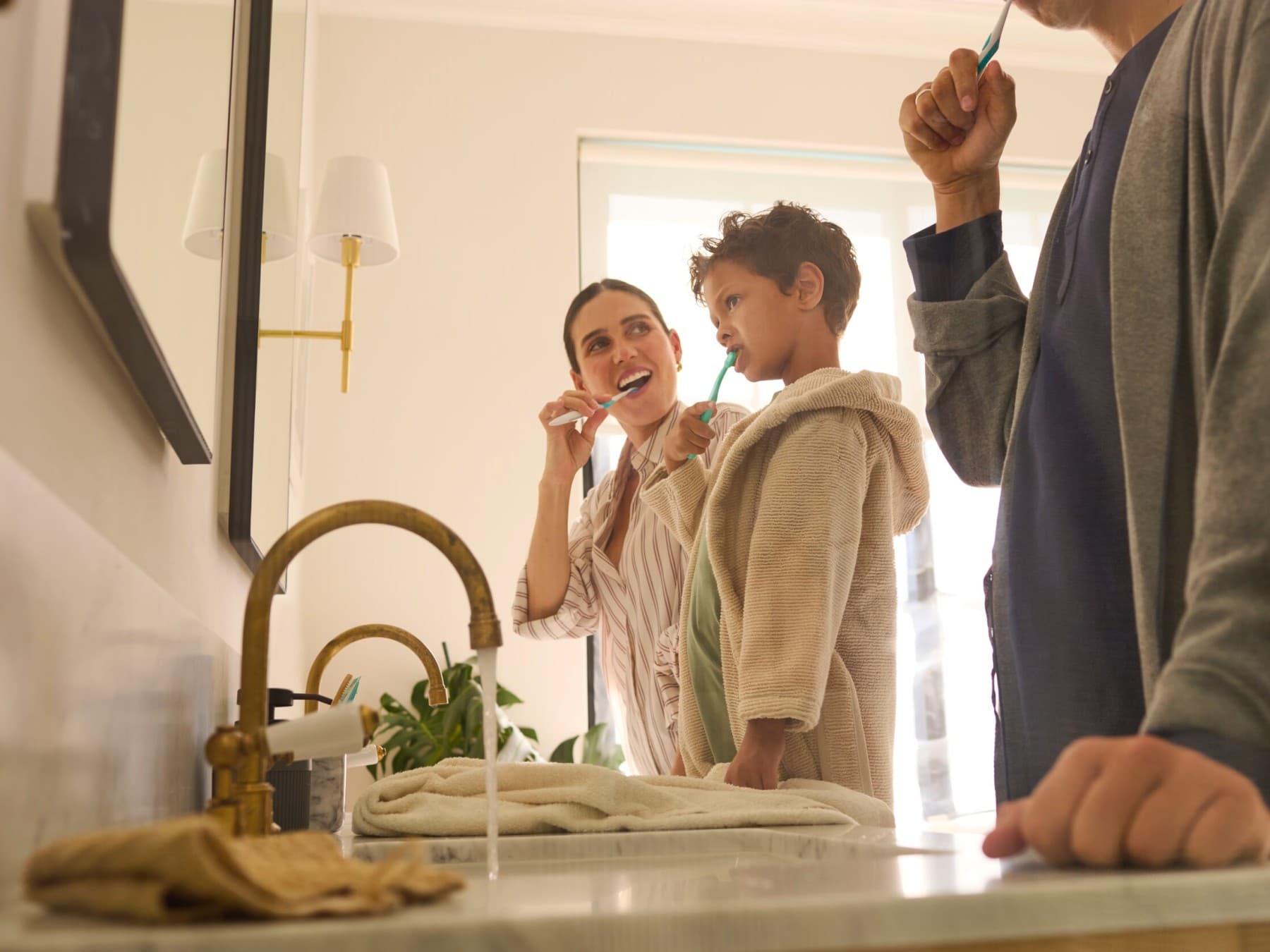 Zwei Erwachsene und ein Kind stehen im Badezimmer vor einem Spiegel und putzen sich die Zähne