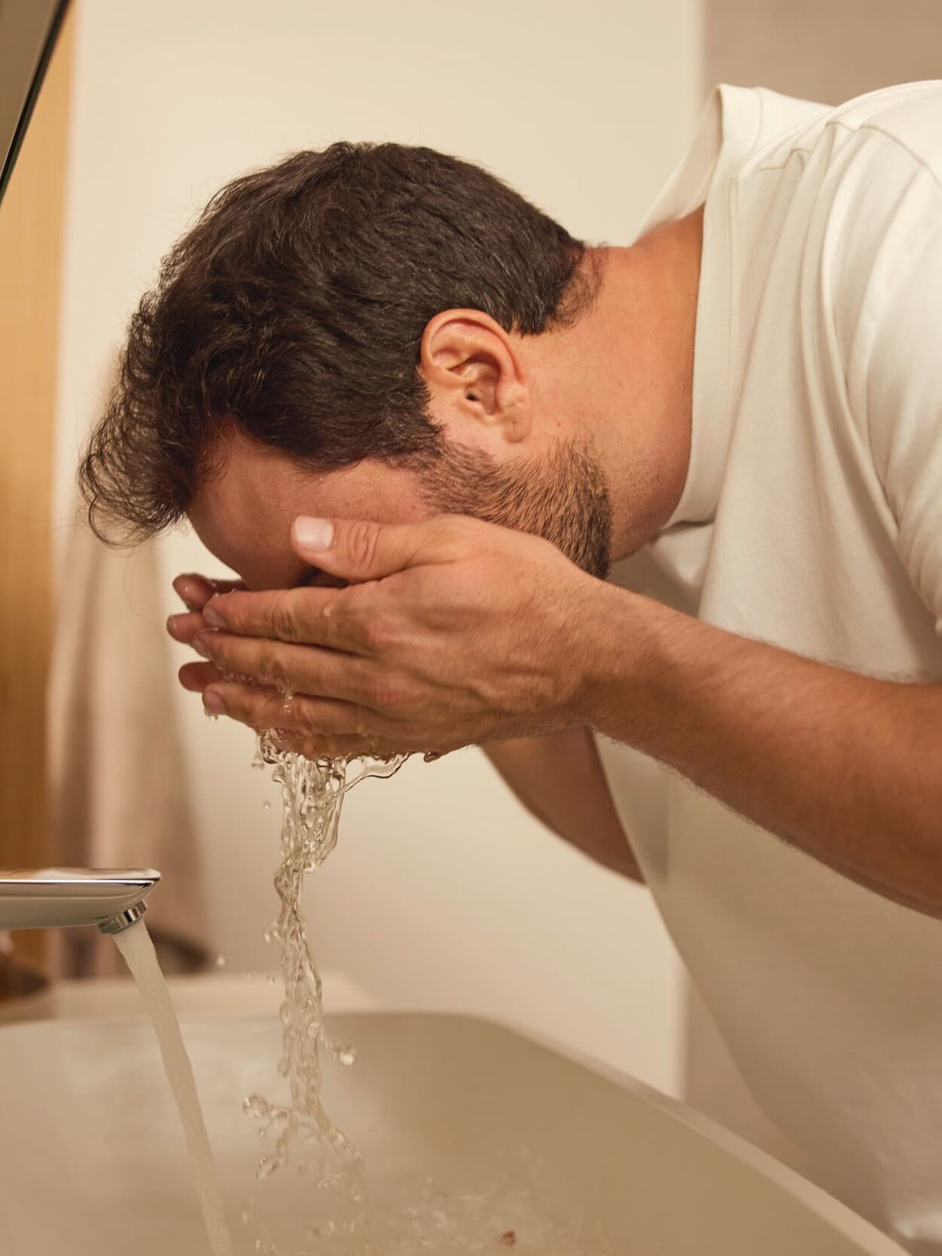 Ein Mann wäscht sich mit Wasser das Gesicht über einem Waschbecken
