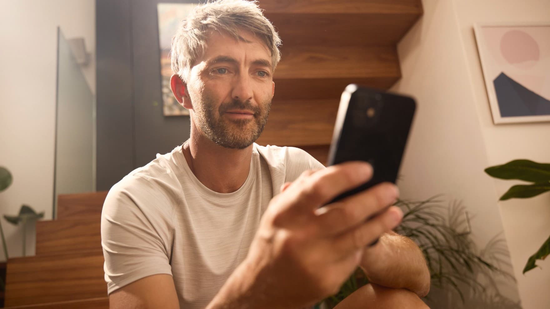 Ein Mann mit einem Smartphone in der Hand steuert seine Heizung via App.