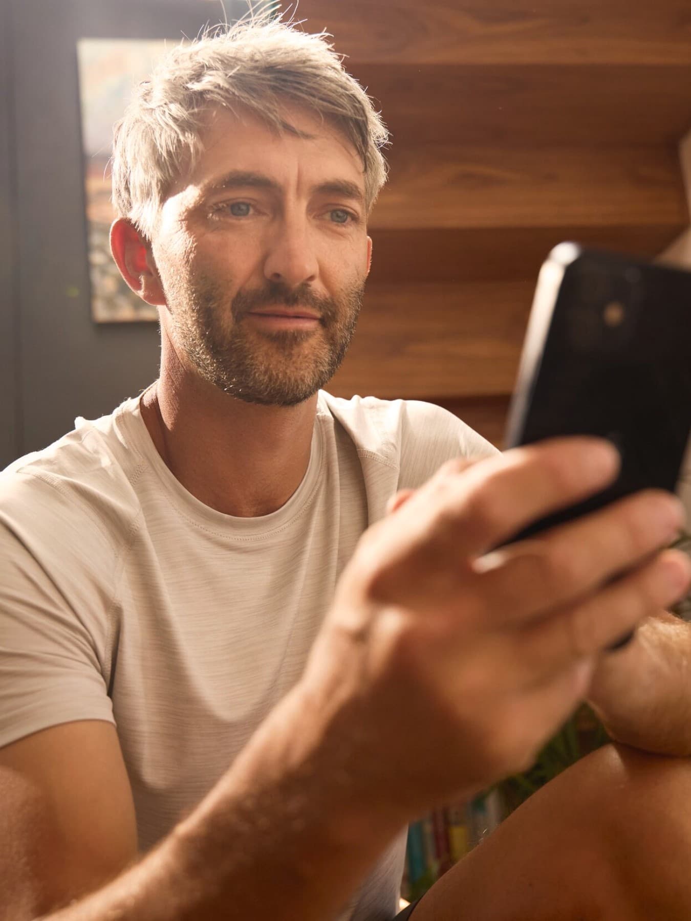 Ein Mann sitzt auf einer Holztreppe in einem Haus und schaut auf sein Smartphone.