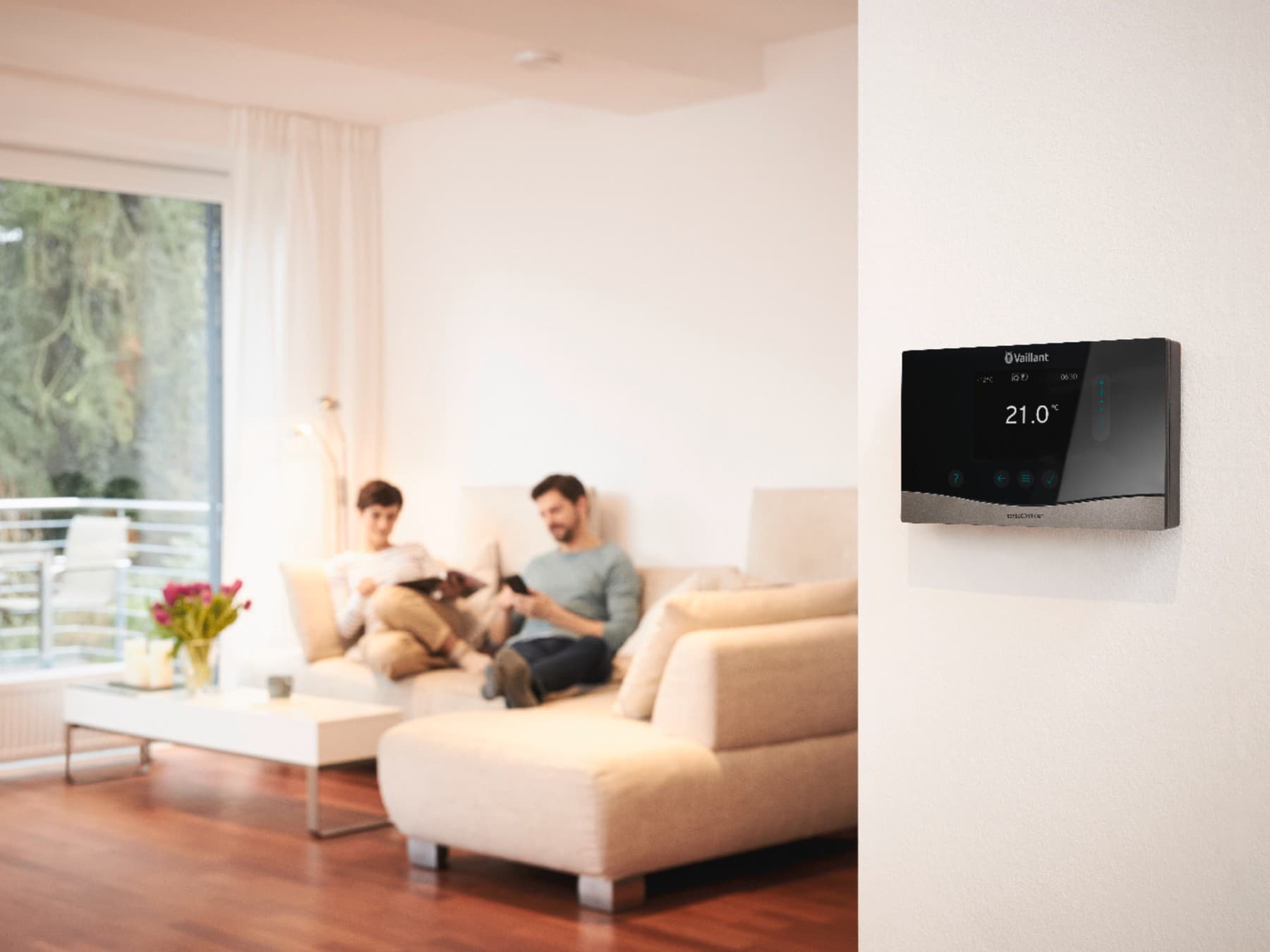 Vaillant Regler an der Wand im Wohnzimmer. Im Hintergrund ist ein Paar auf der Couch zu sehen.