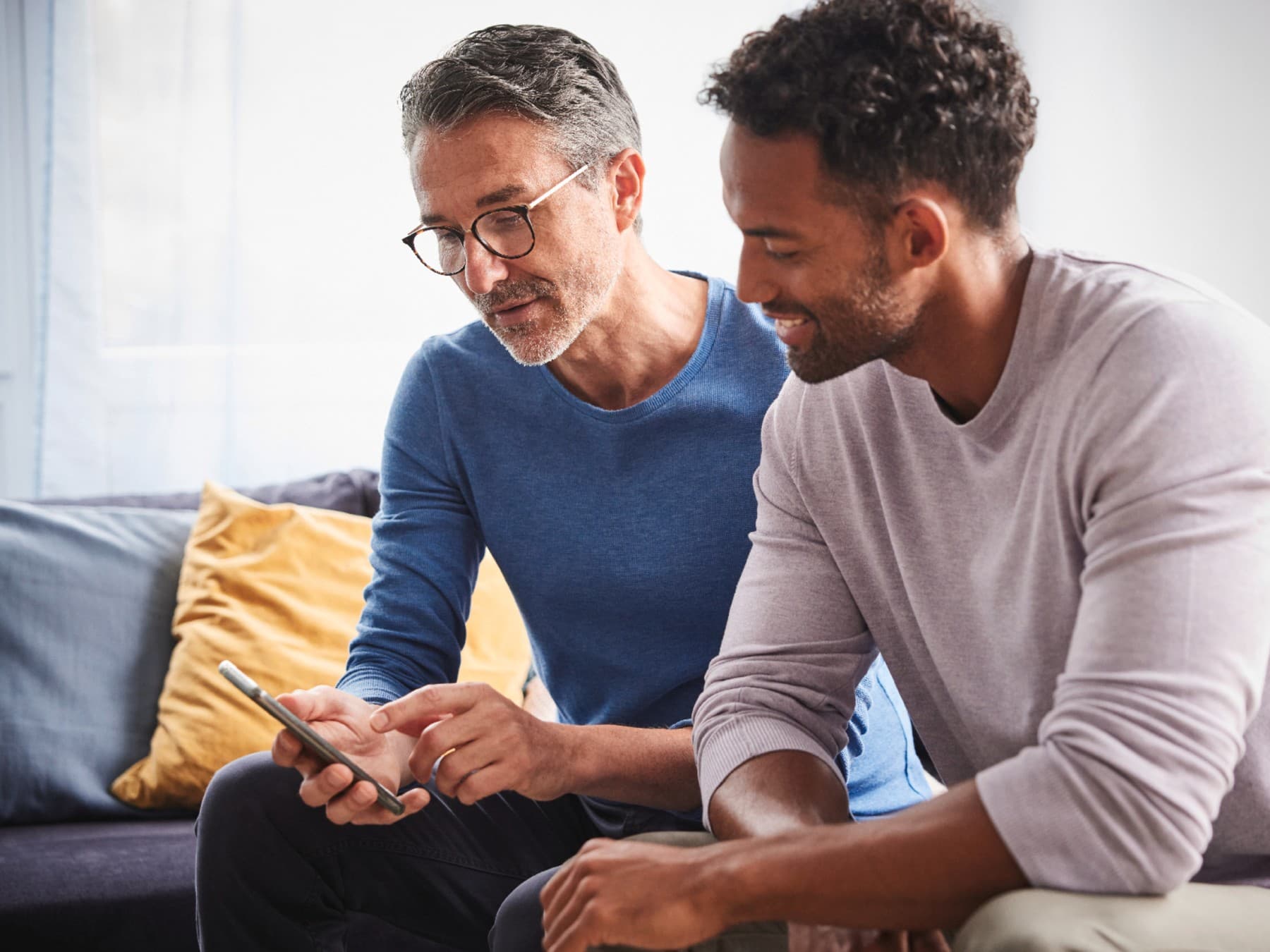 Bild von zwei Männern auf einer Couch, die auf ein Smartphone gucken