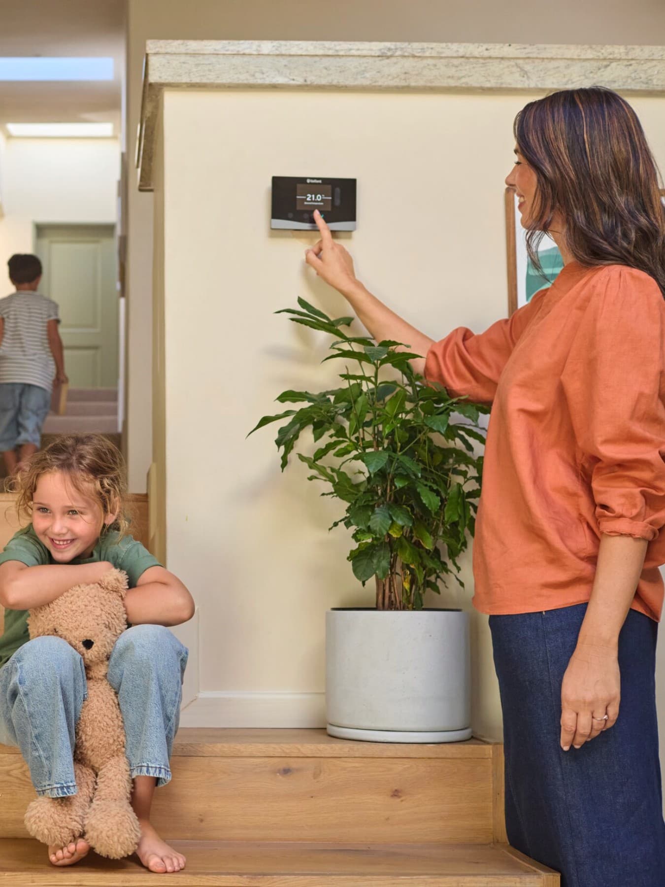 Eine junge Frau steht am Heizungsthermostat im Flur neben der Treppe und stellt die richtige Raumtemperatur ein.