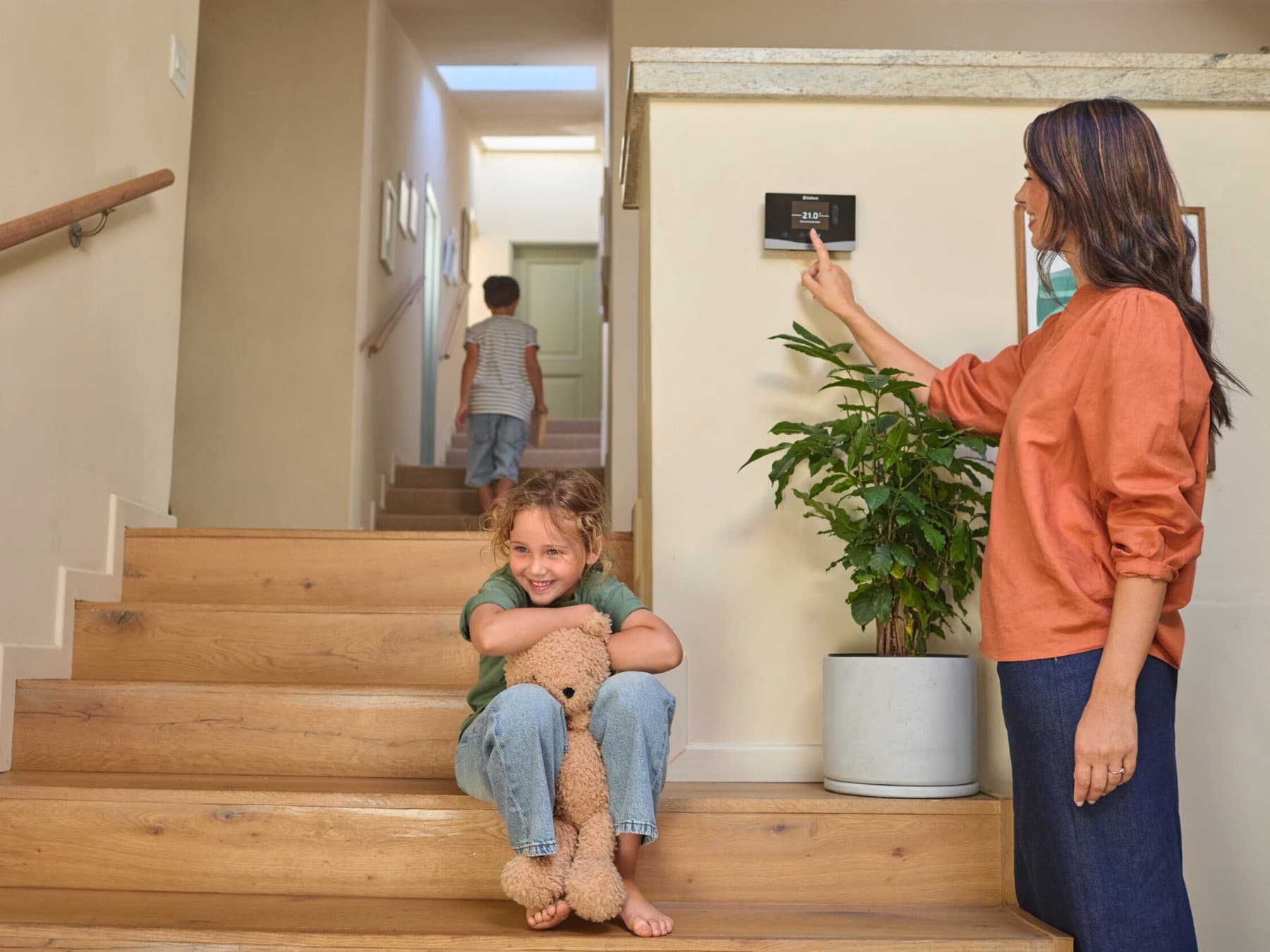 Frau bedient Regler im Wohnbereich, zwei Kinder sind auf der Treppe zu sehen.
