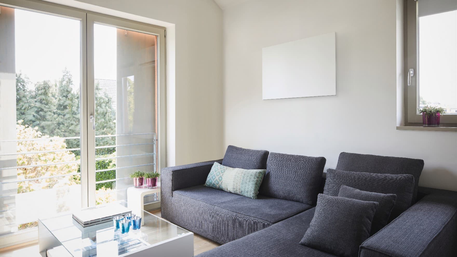 Eine Infrarotheizung von Vaillant hängt in einem hellen Wohnzimmer über einer Couch wie ein Bild an der Wand.