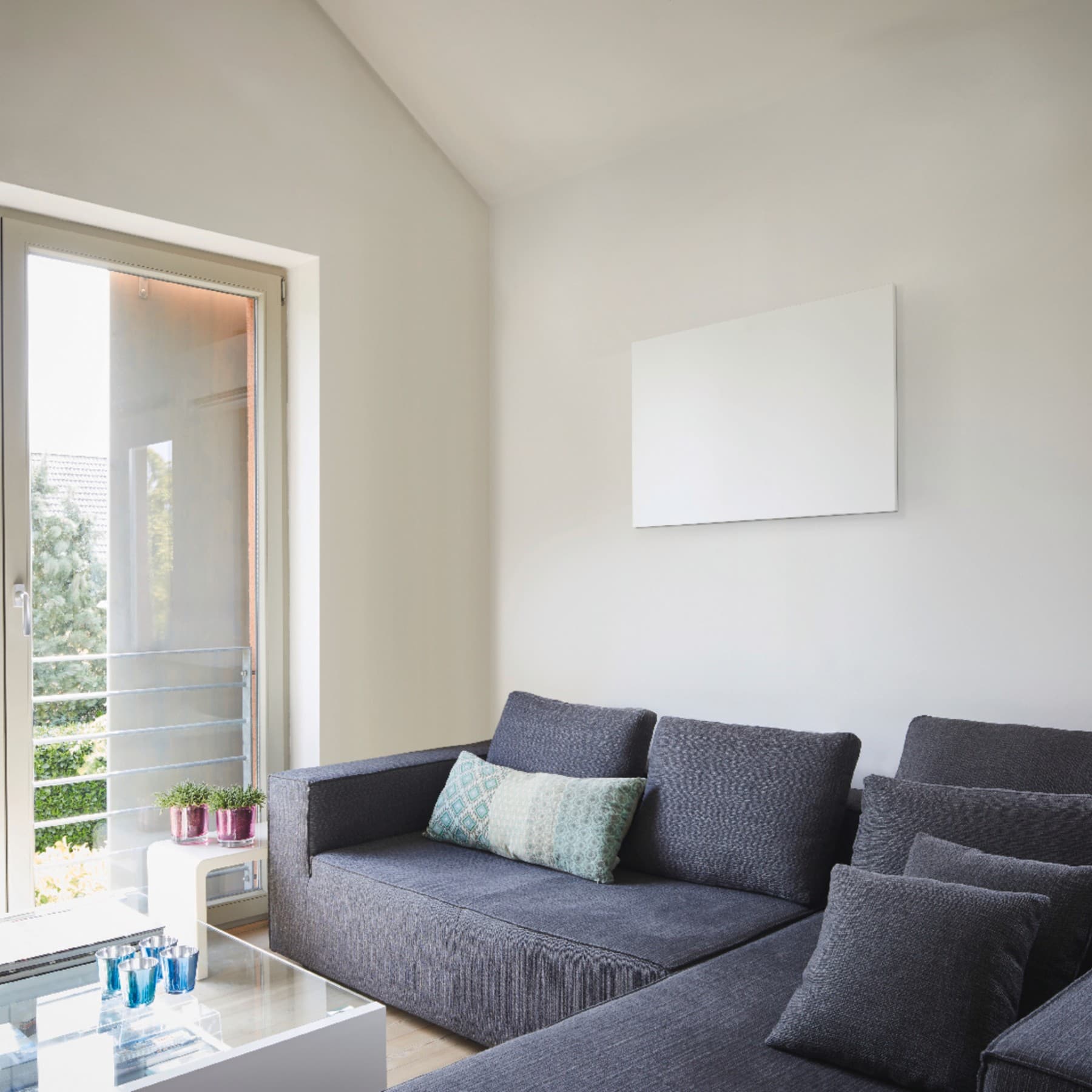 Infrarotheizung an der Wohnzimmerwand, im Vordergrund eine Couch, auf der linken Seite eine Fensterfront