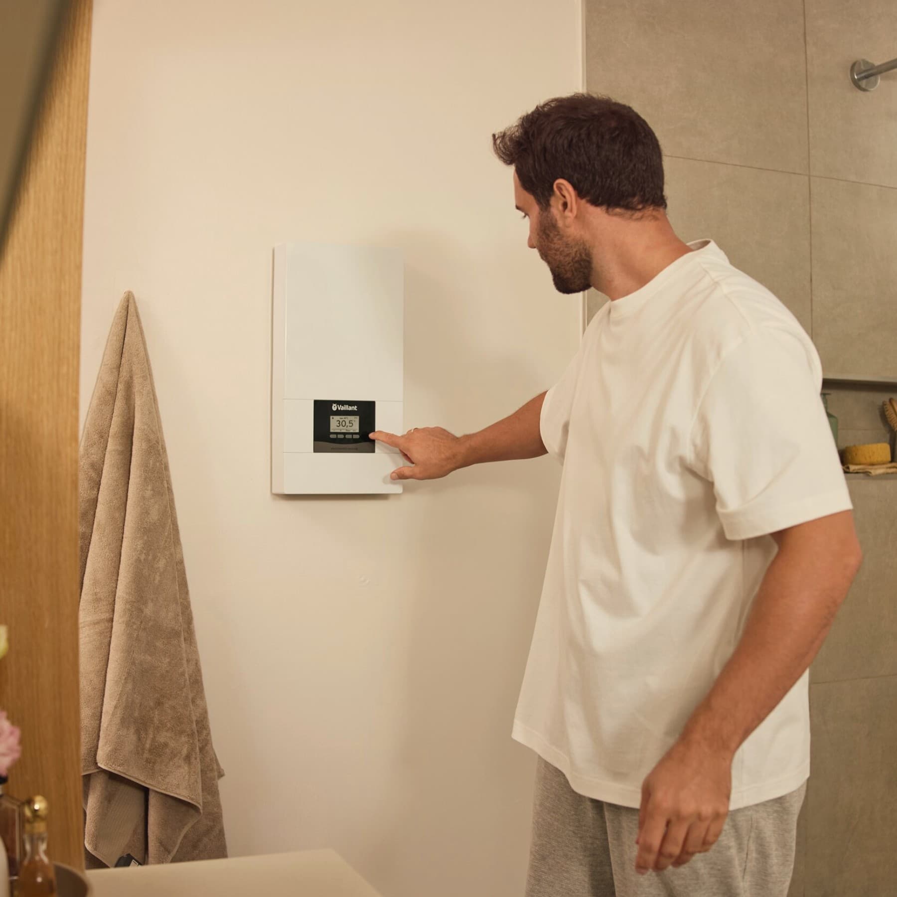 Ein Mann bedient einen an einer Badezimmer-Wand hängenden Durchlauferhitzer Vaillant electronicVED