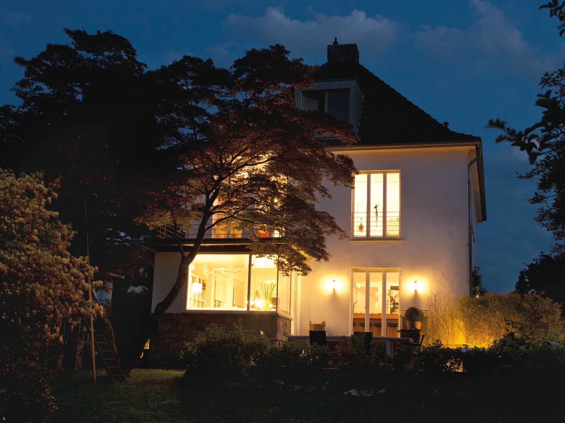 Älteres freistehendes Einfamilienhaus bei Dunkelheit mit hell erleuchteten Fenstern