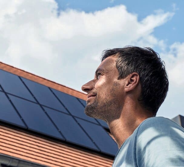 Ein Mann steht vor einem Haus mit Photovoltaik-Anlage und schaut in den Himmel.