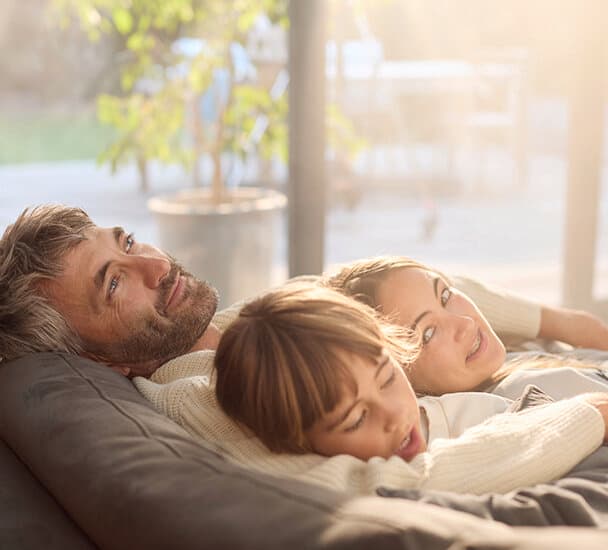 Ein Mann liegt mit zwei Kindern im Arm gemütlich auf einer Couch.