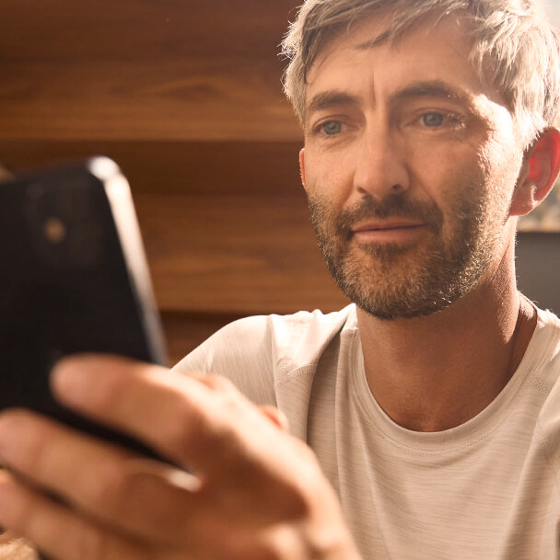 Ein Mann in Nahaufnahme, der ein Smartphone in der linken Hand hält, auf das er schaut.