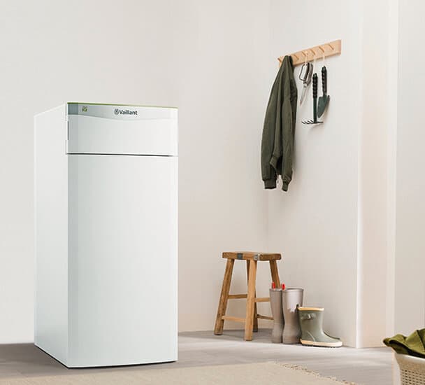 Eine Vaillant flexoTHERM exclusive steht in einem Flur neben einer Garderobe, an der eine Jacke hängt. Darunter stehen Gummistiefel und ein Schemel.