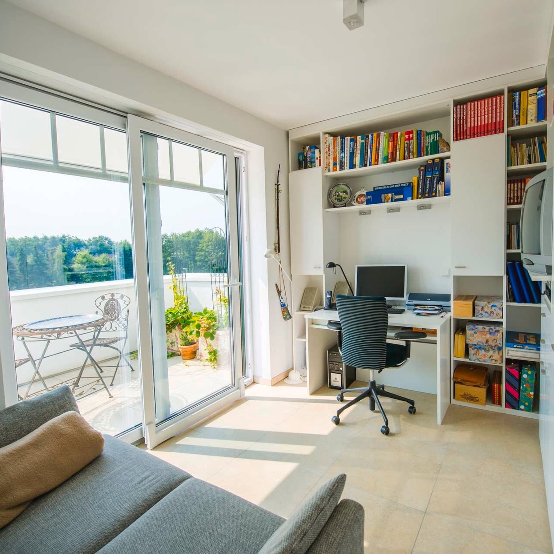 Innenansicht des Wohnzimmers mit Couch, Schreibtisch und angrenzendem Balkon
