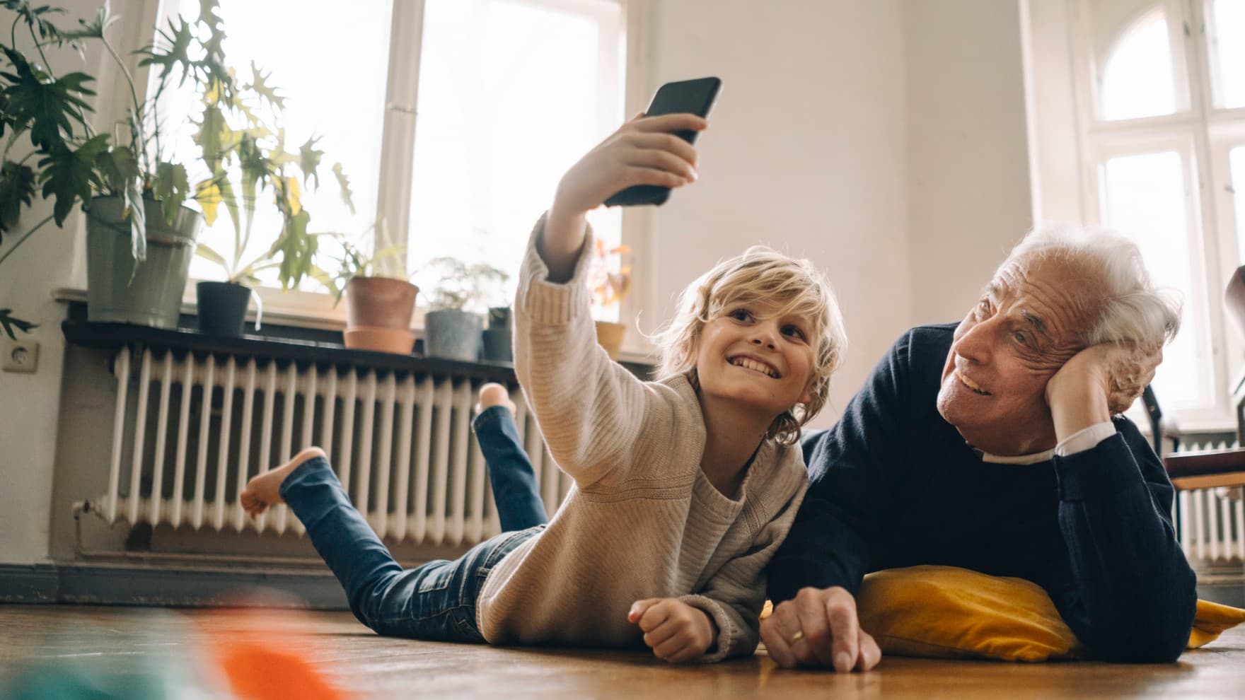 Ein Junge liegt mit seinem Opa vor dem Heizkörper und macht ein Selfie.