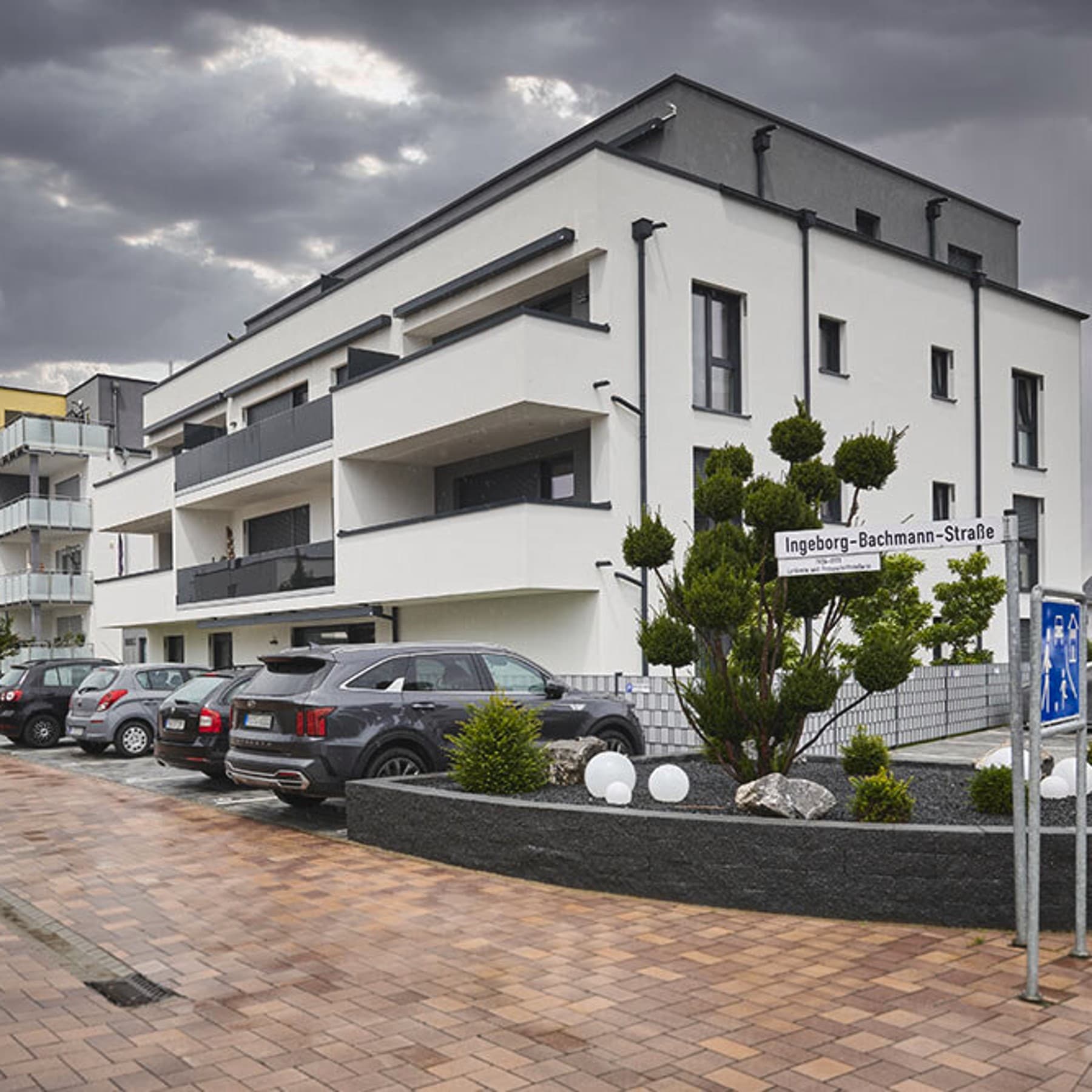 Außenansicht des Mehrfamilienhauses, im Vordergrund parken Autos auf Stellplätzen