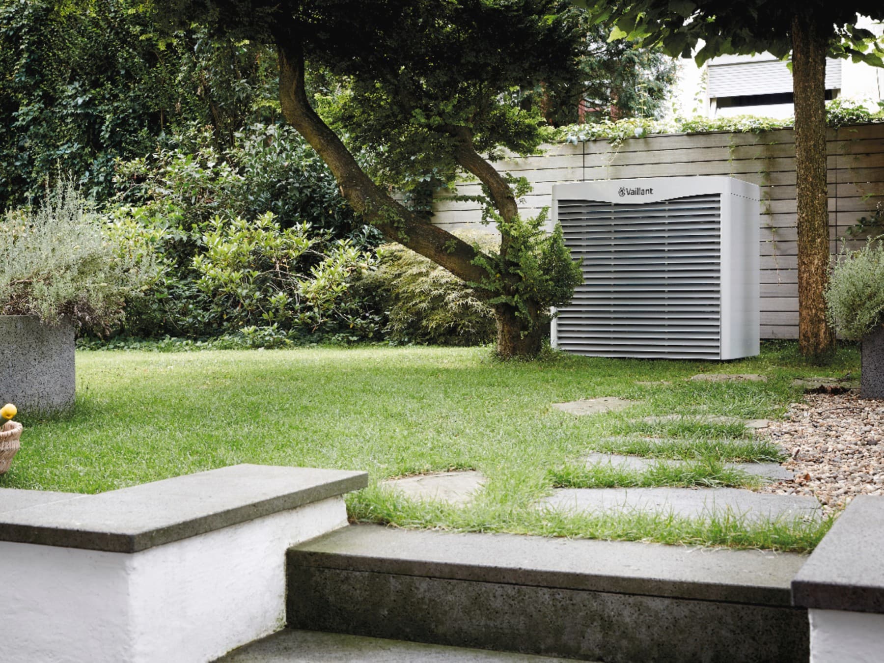 Luft-Sole-Kollektor aroCOLLECT von Vaillant steht im grünem Garten zwischen zwei Bäumen