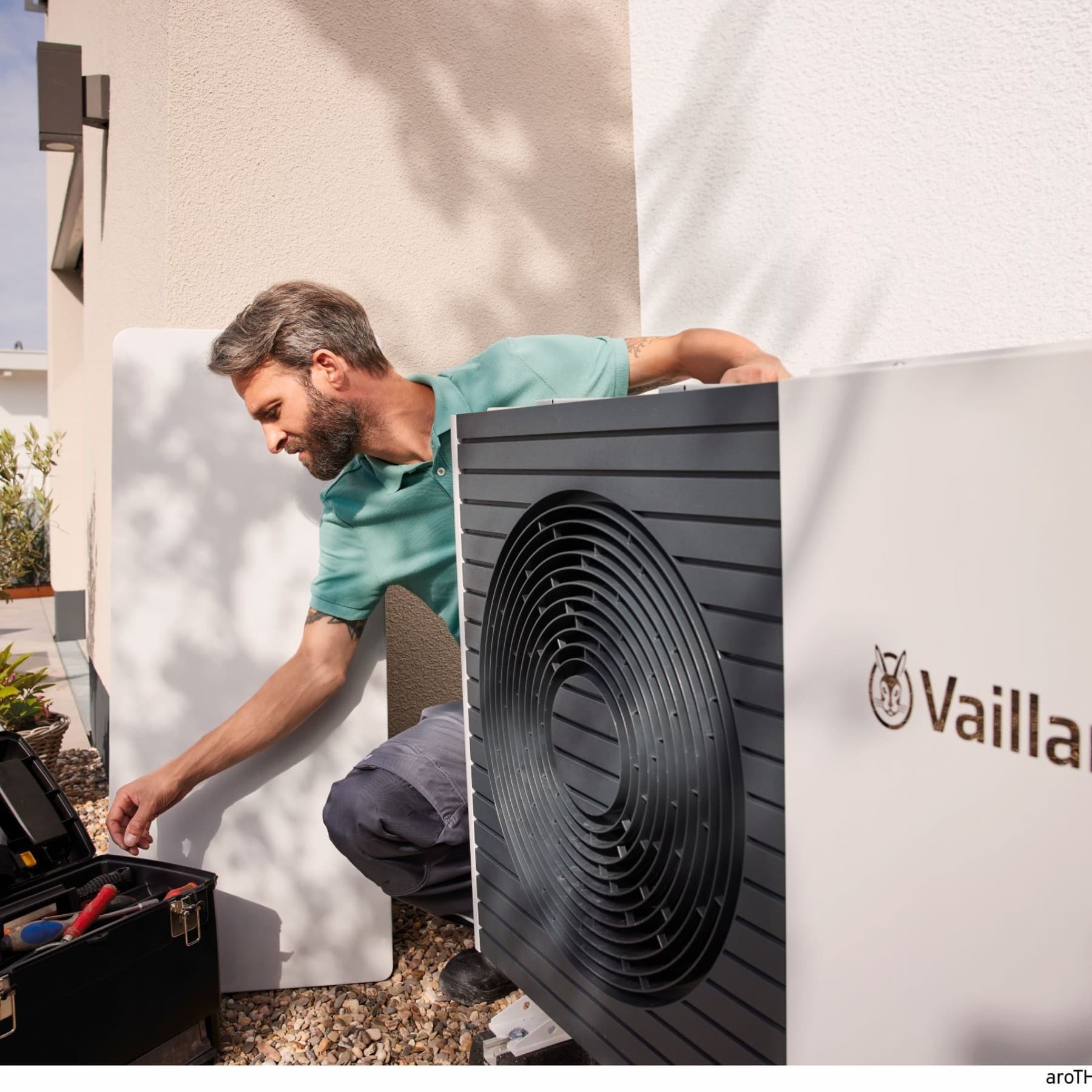 Fachhandwerker installiert eine Split-Wärmepumpe aroTHERM Split plus von Vaillant neben einem Neubau