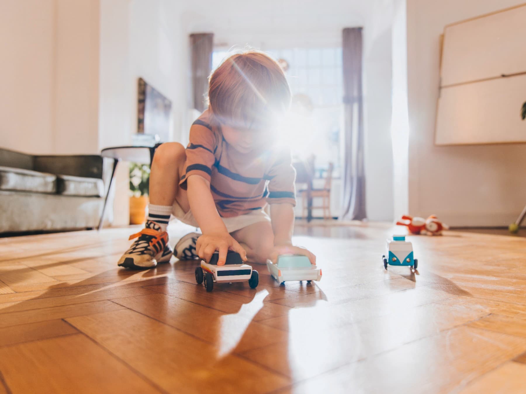 Ein Kind spielt mit Spielzeugautos auf einem Holzußboden in einem Wohnzimmer.