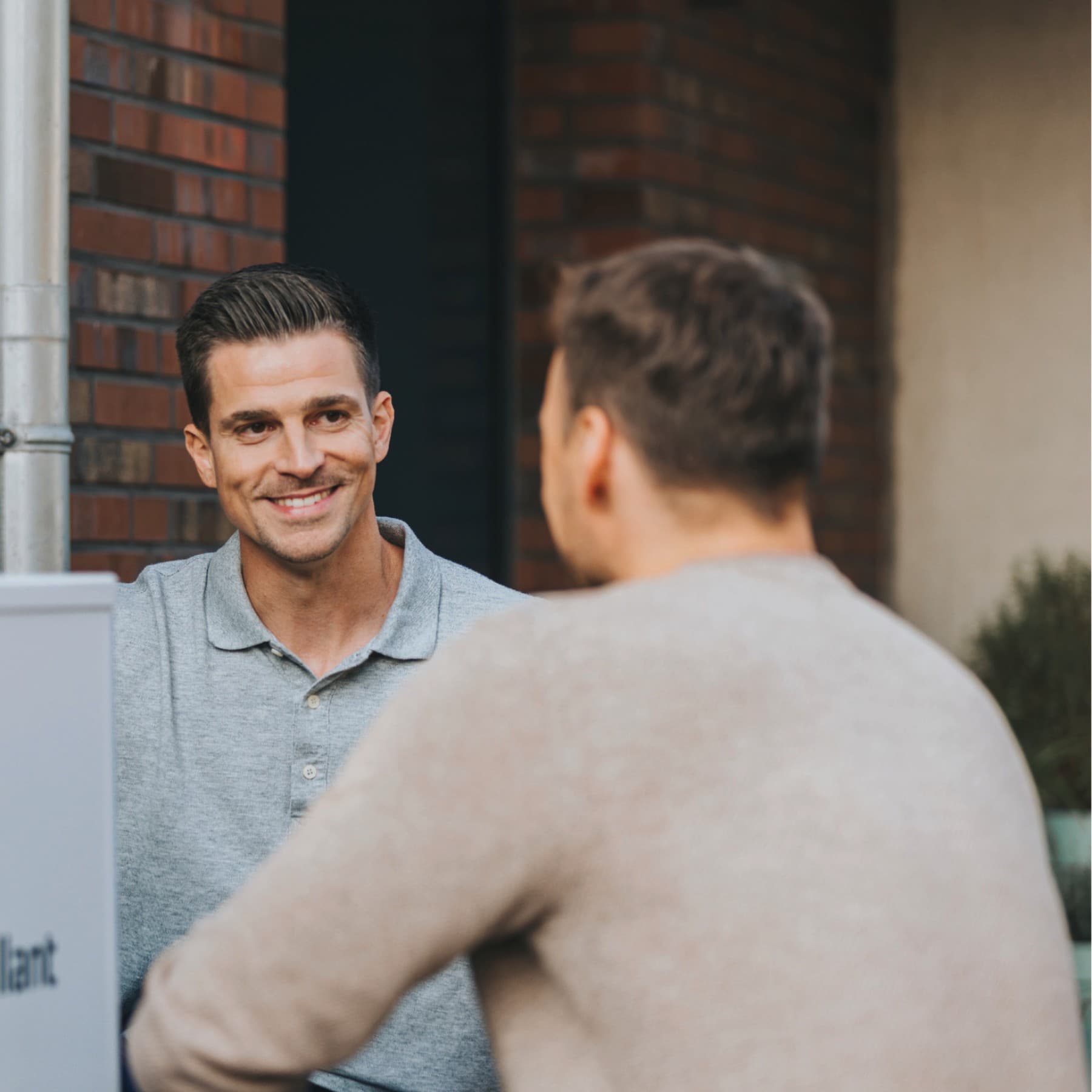 Ein Vaillant Fachhandwerker und ein Kunde hocken neben einer Vaillant Wärmepumpe und schauen sich an.