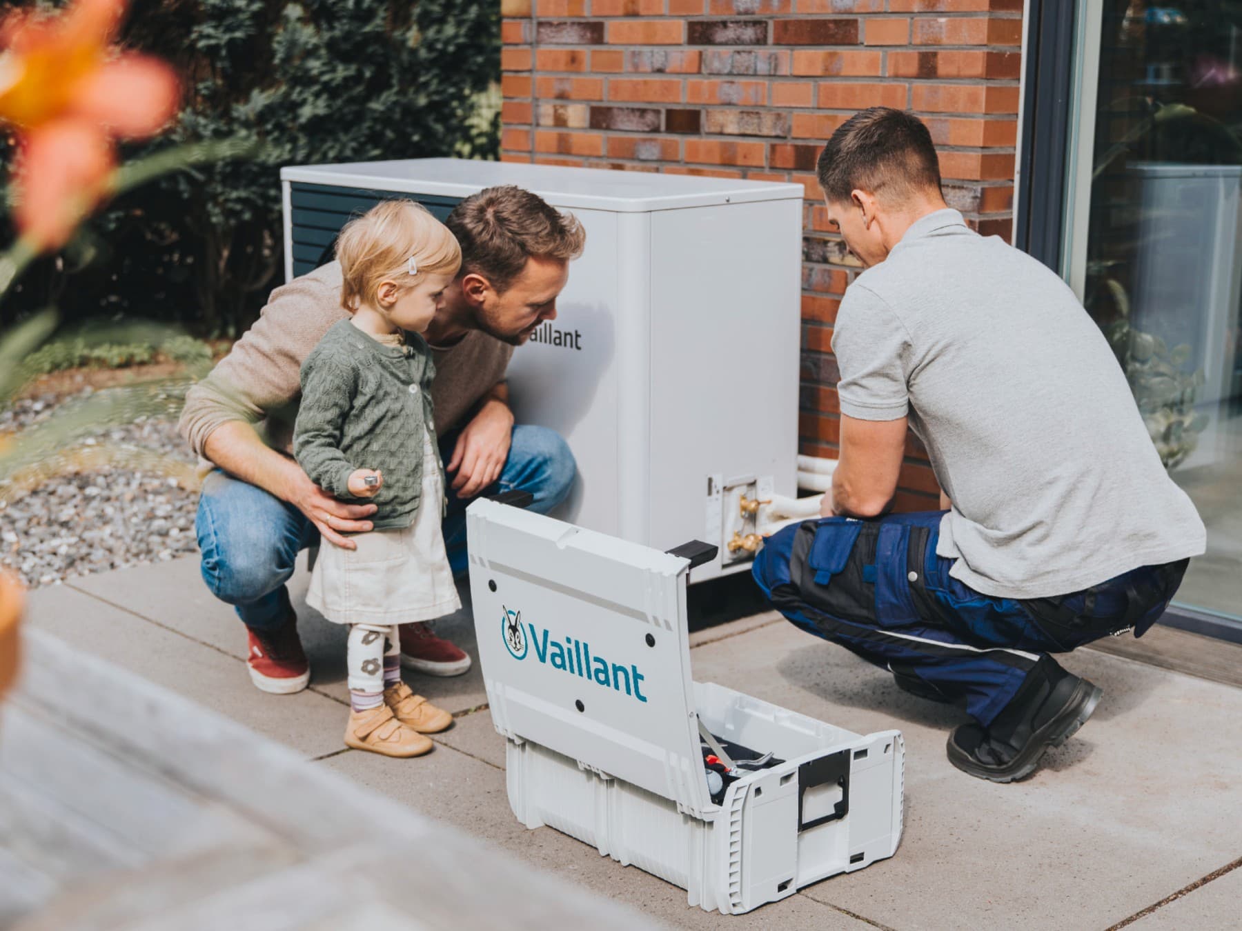 Ein Vater und seine Tochter beobachten, wie ein Fachhandwerker eine Wärmepumpe installiert