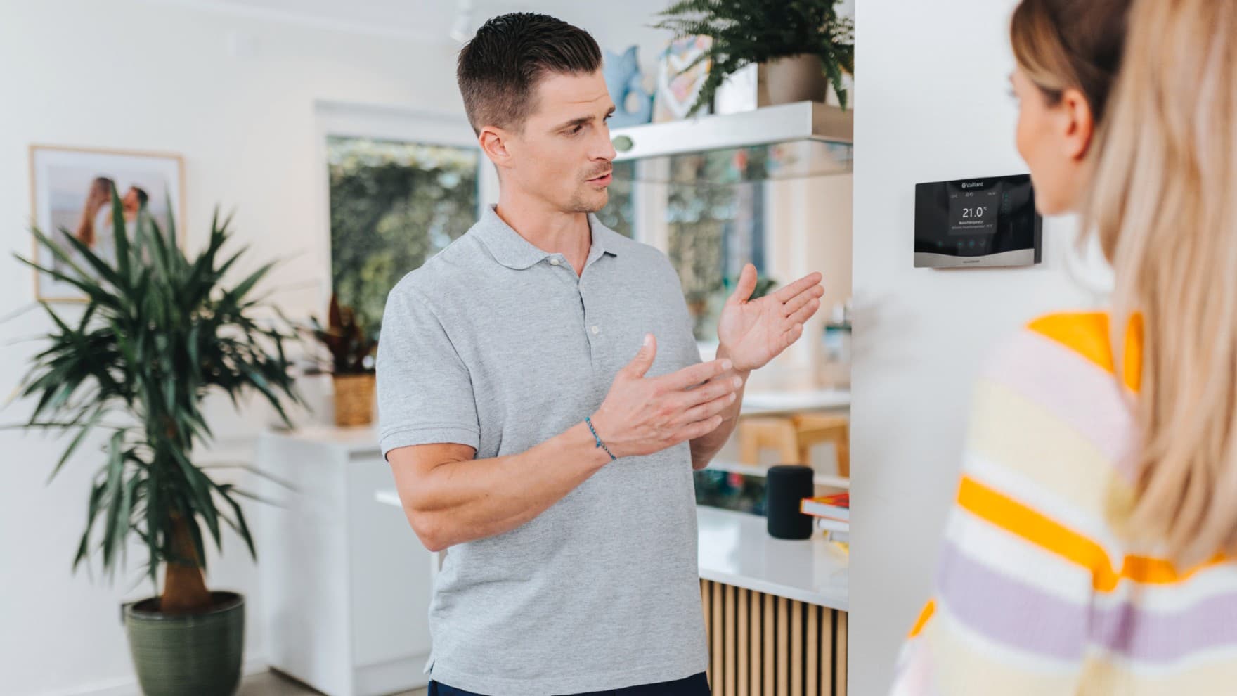Ein Installateur erklärt einer Hausbesitzerin die Heizungsregelung an der Wand