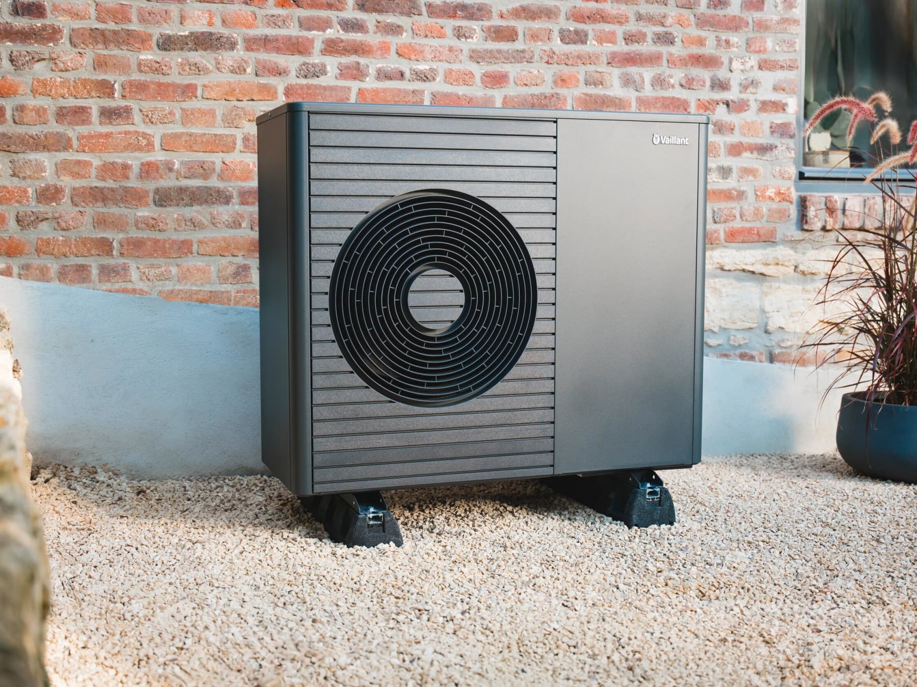 Eine Vaillant Wärmepumpe mit einem Lüfter steht außen vor einer Ziegelwand.
