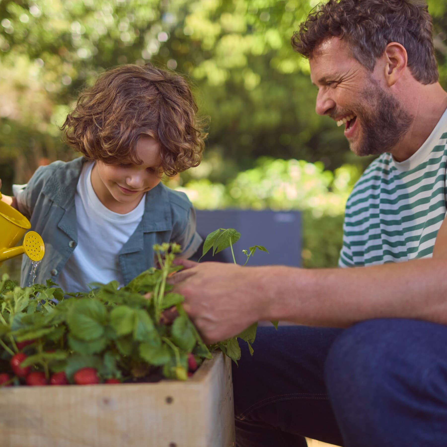 Ein Mann schaut einem Kind fröhlich beim Pflanzen gießen zu. Im Hintergrund steht eine schwarzgraue Vaillant Wärmepumpe im Garten.
