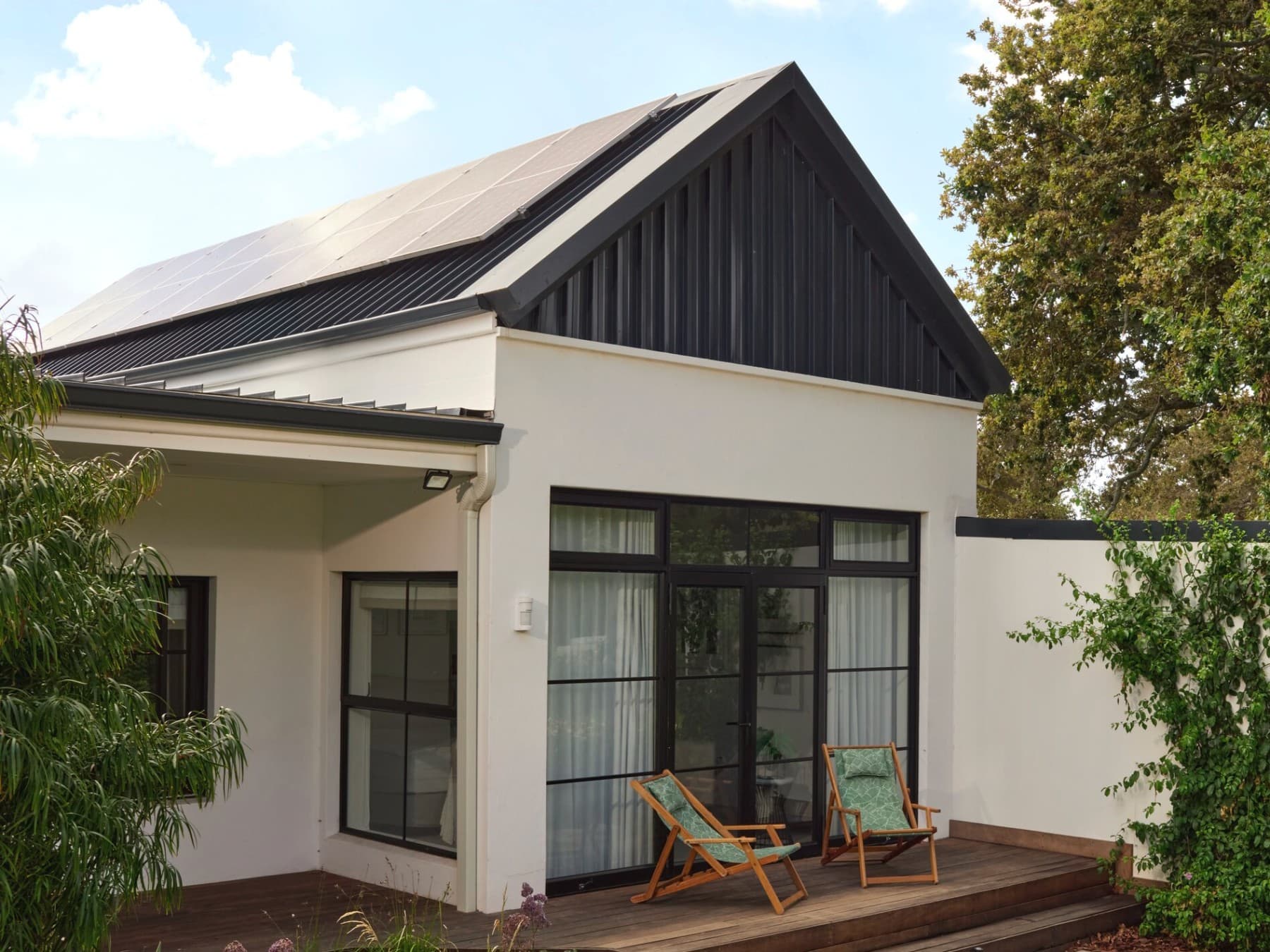 Kleines Haus mit einer Veranda vorne und PV-Modulen auf dem Dach.