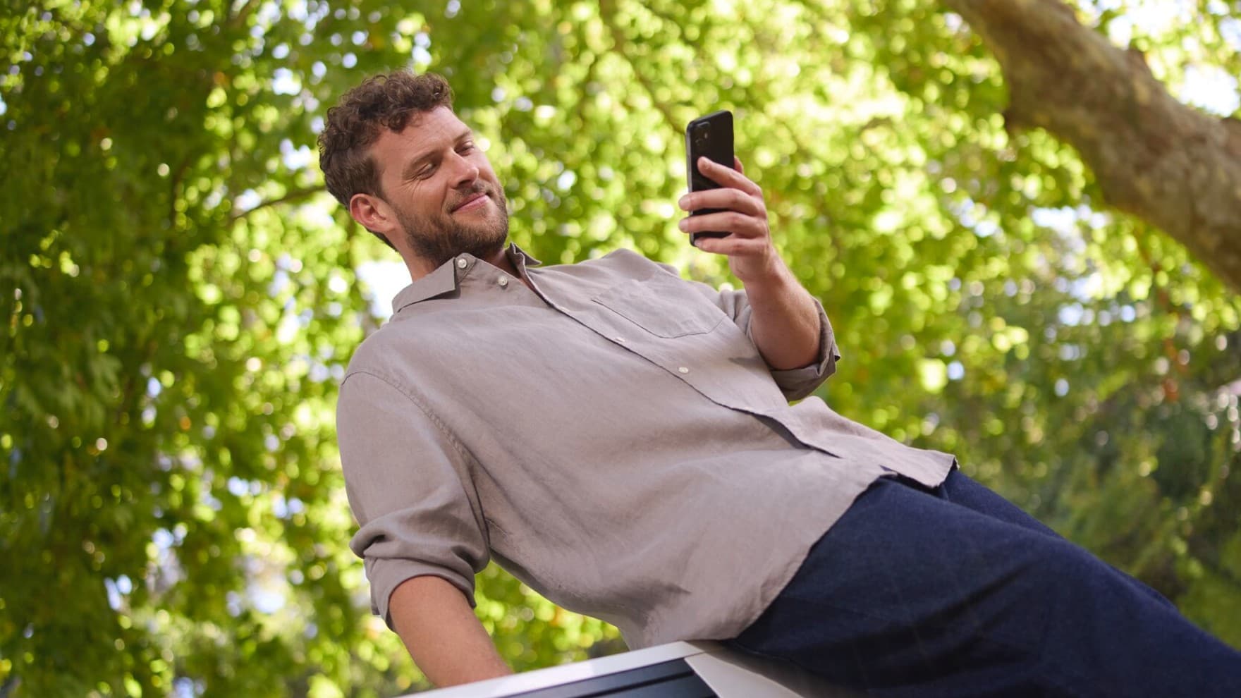 Mann steht draußen im Garten, hält sein Handy in der Hand und schaut dabei in die myVaillant App.
