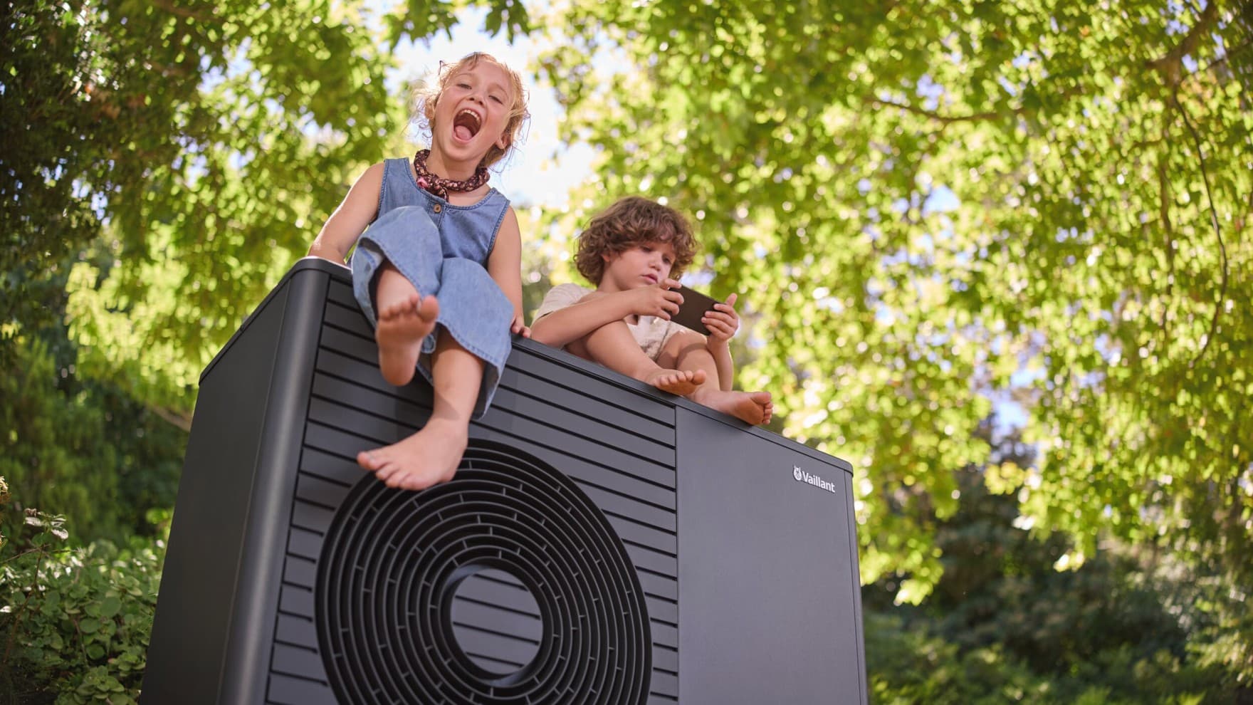 Zwei Kinder sitzen auf einer Vaillant aroTHERM plus Wärmepumpe.