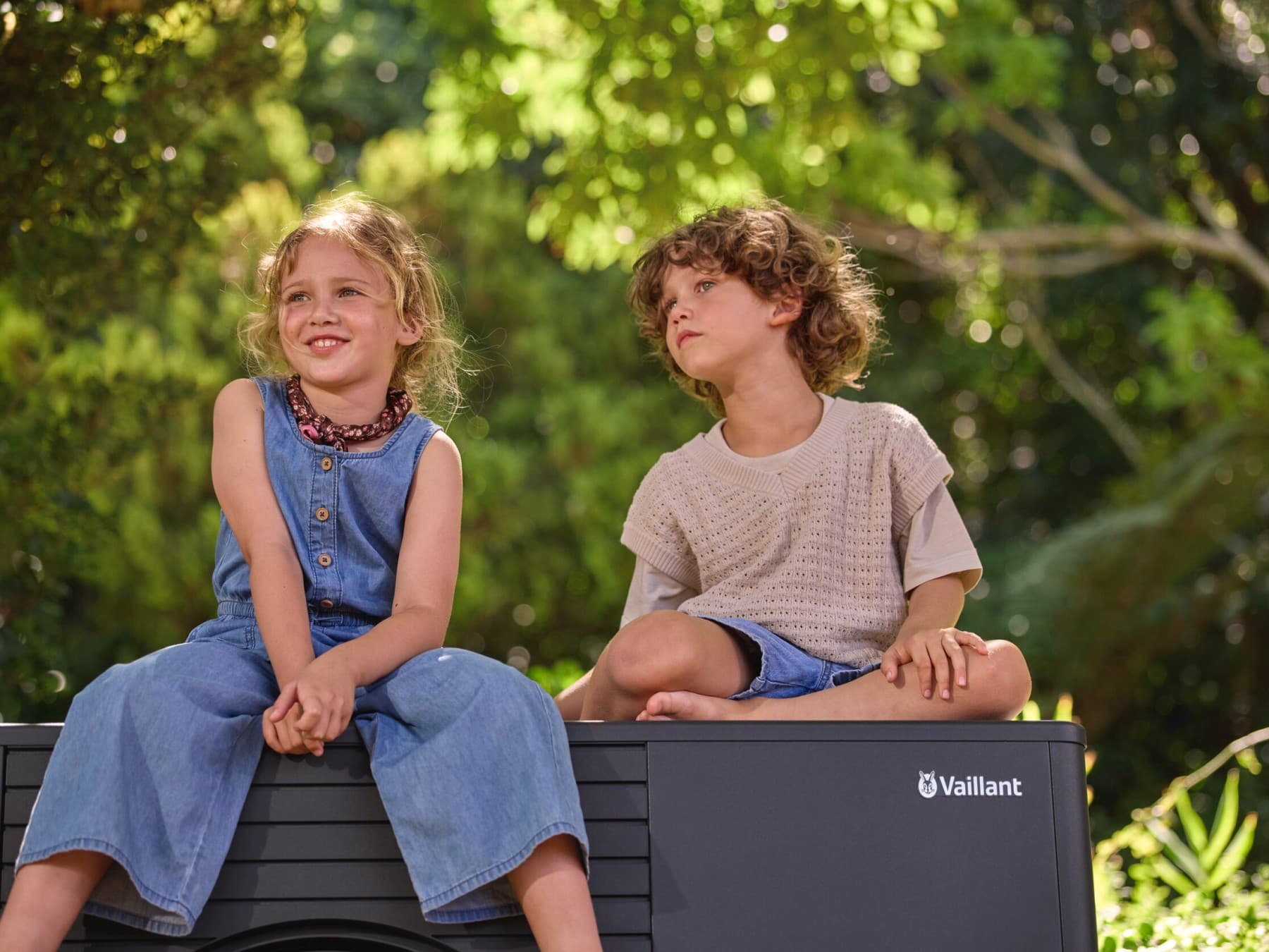Zwei kleine Kinder sitzen auf einer Wärmepumpe im Garten