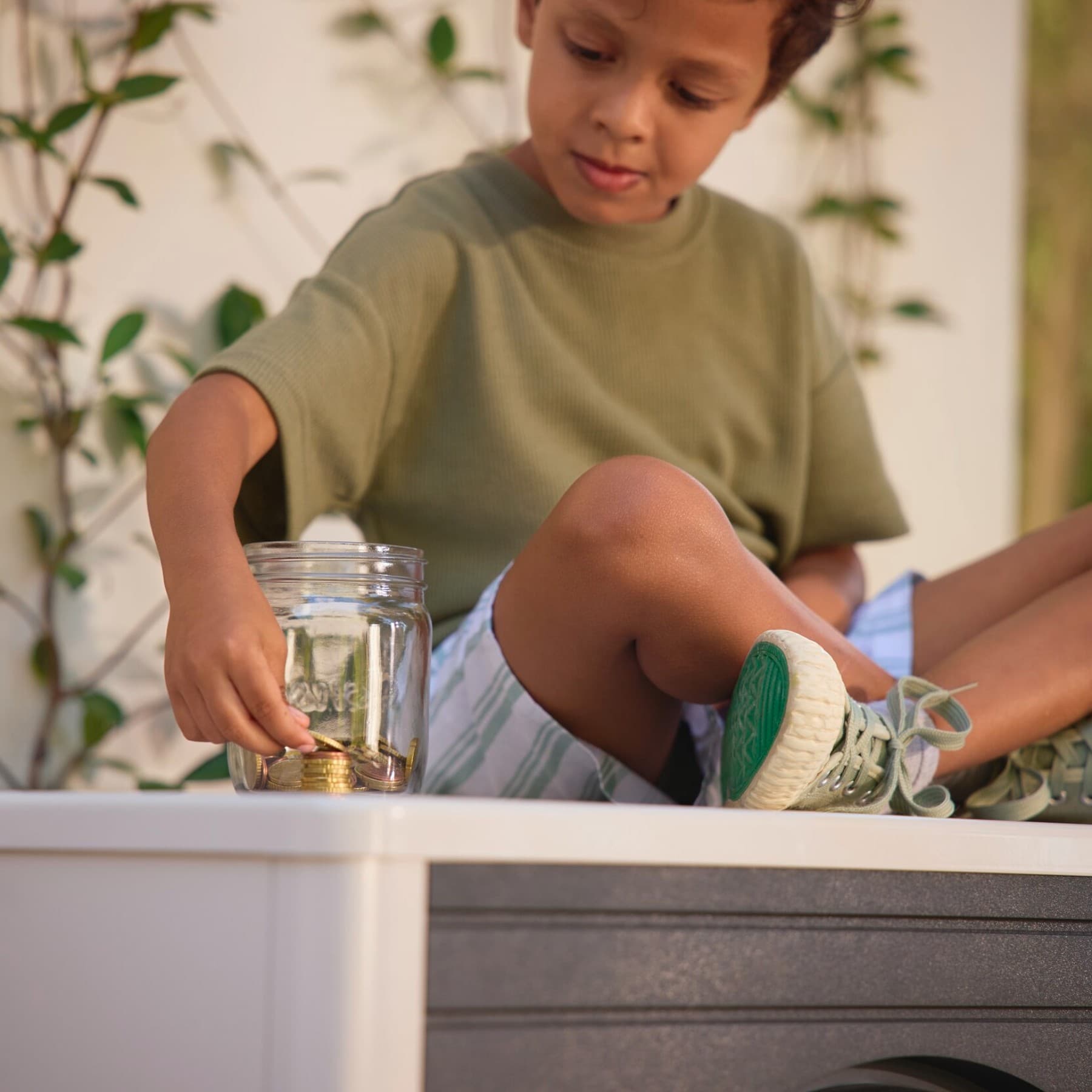 Ein Junge sitzt auf einer Vaillant Wärmepumpe und stapelt Münzen neben einem Einmachglas