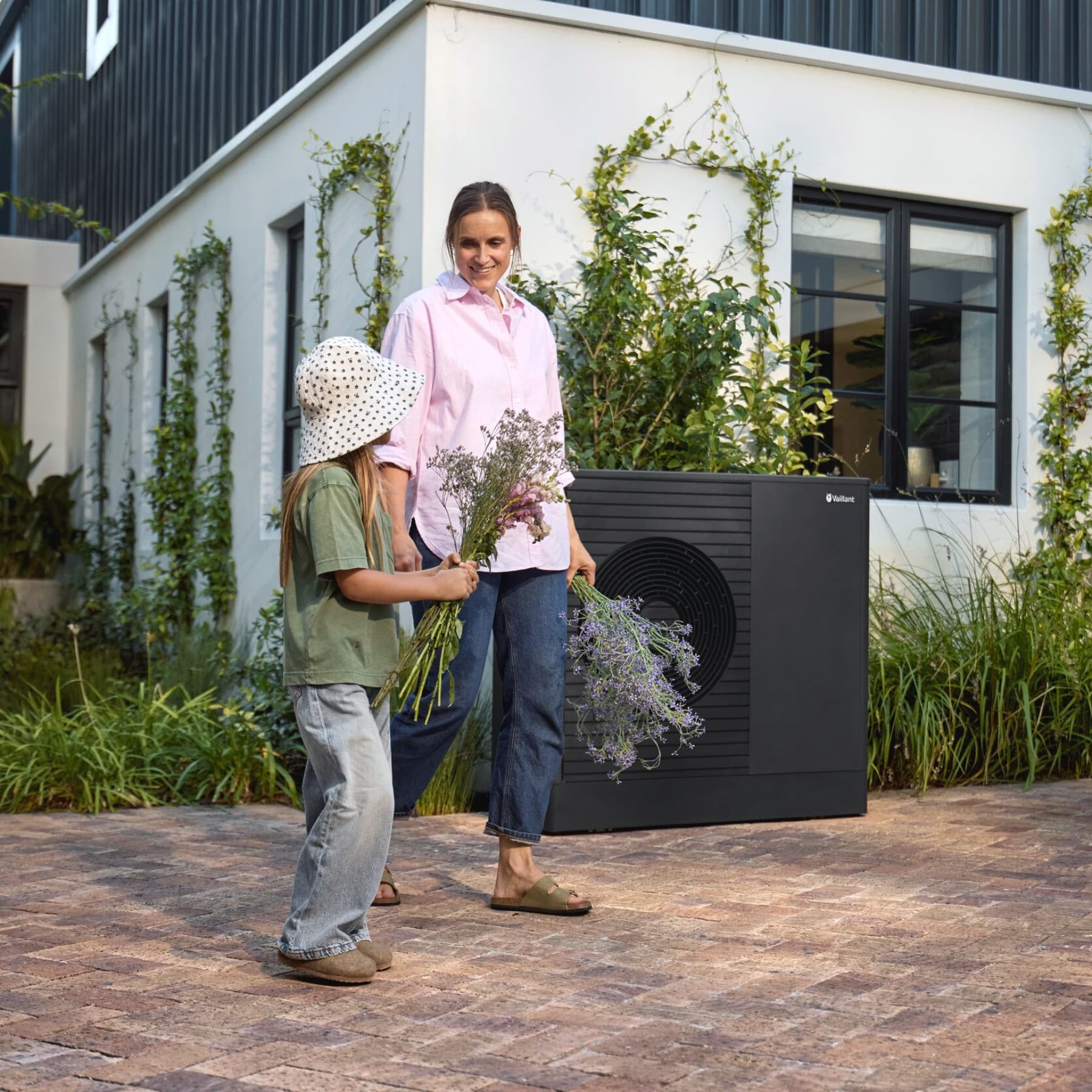Frau und Kind vor einer Vaillant Wärmepumpe aroTHERM plus im Garten eines Einfamlienhauses