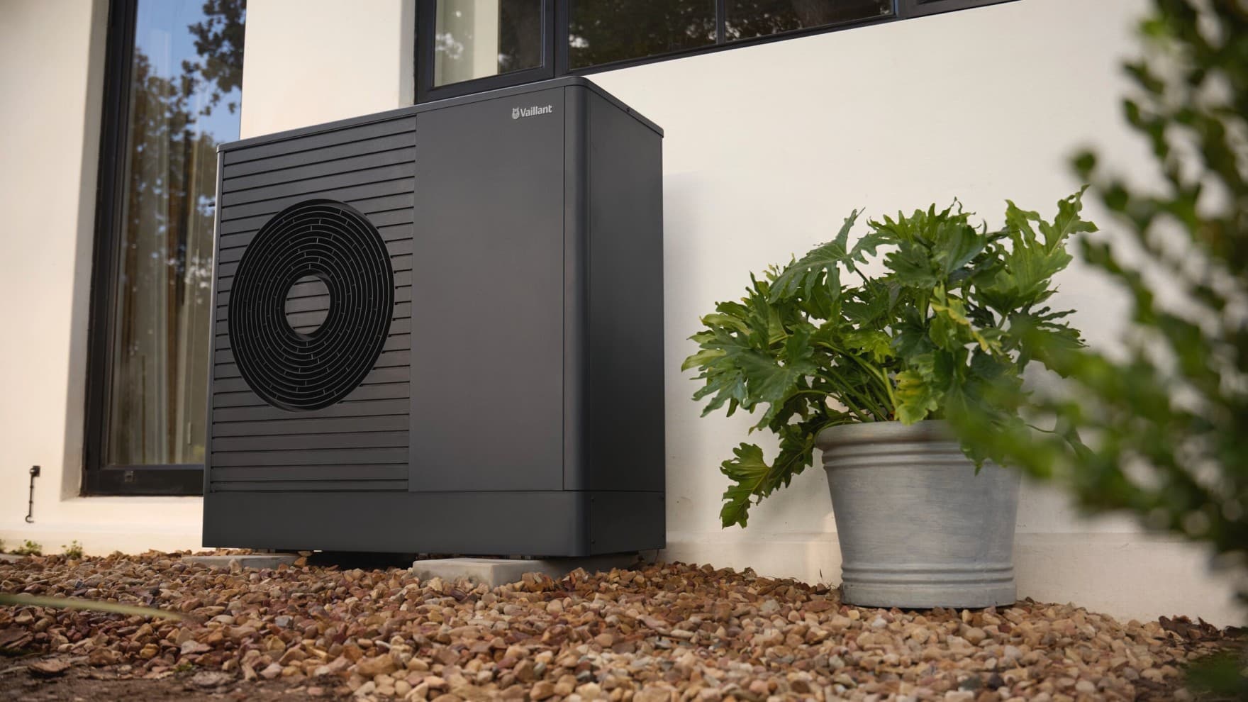 Außeneinheit der Luft-Wasser-Wärmepumpe aroTHERM plus von Vaillant an einer Hauswand im Garten