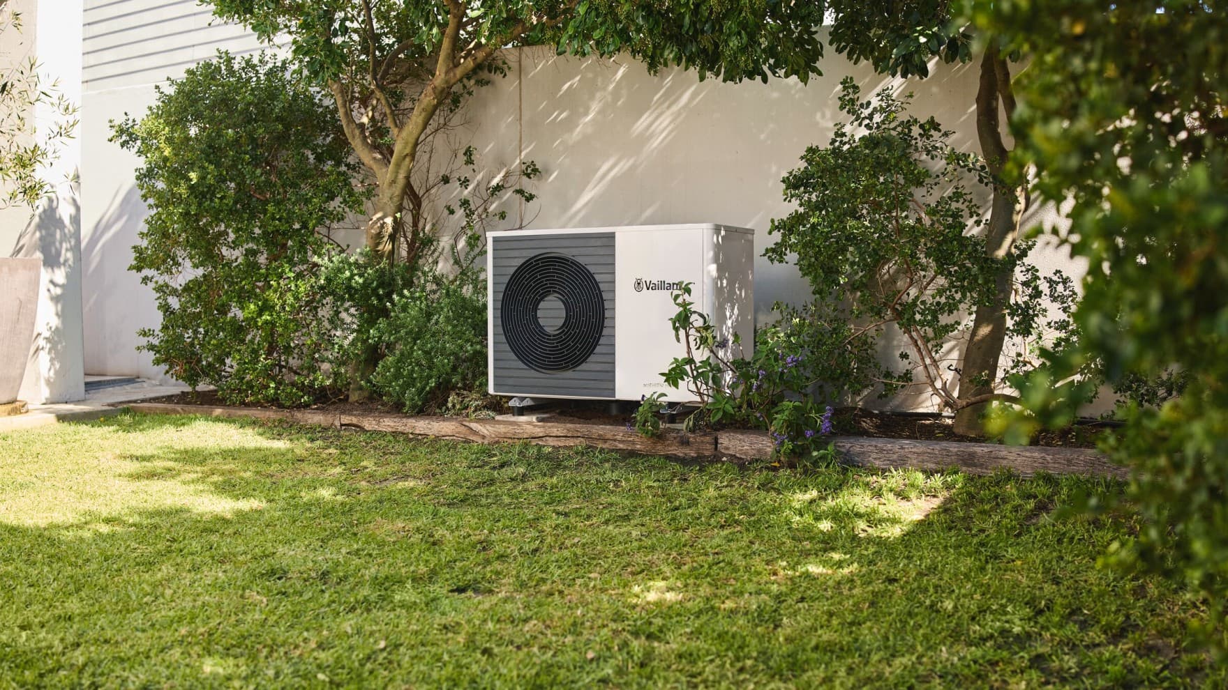 Weiße Luft/Wasser-Wärmepumpe aroTHERM Split steht unauffällig im sommerlichen Garten