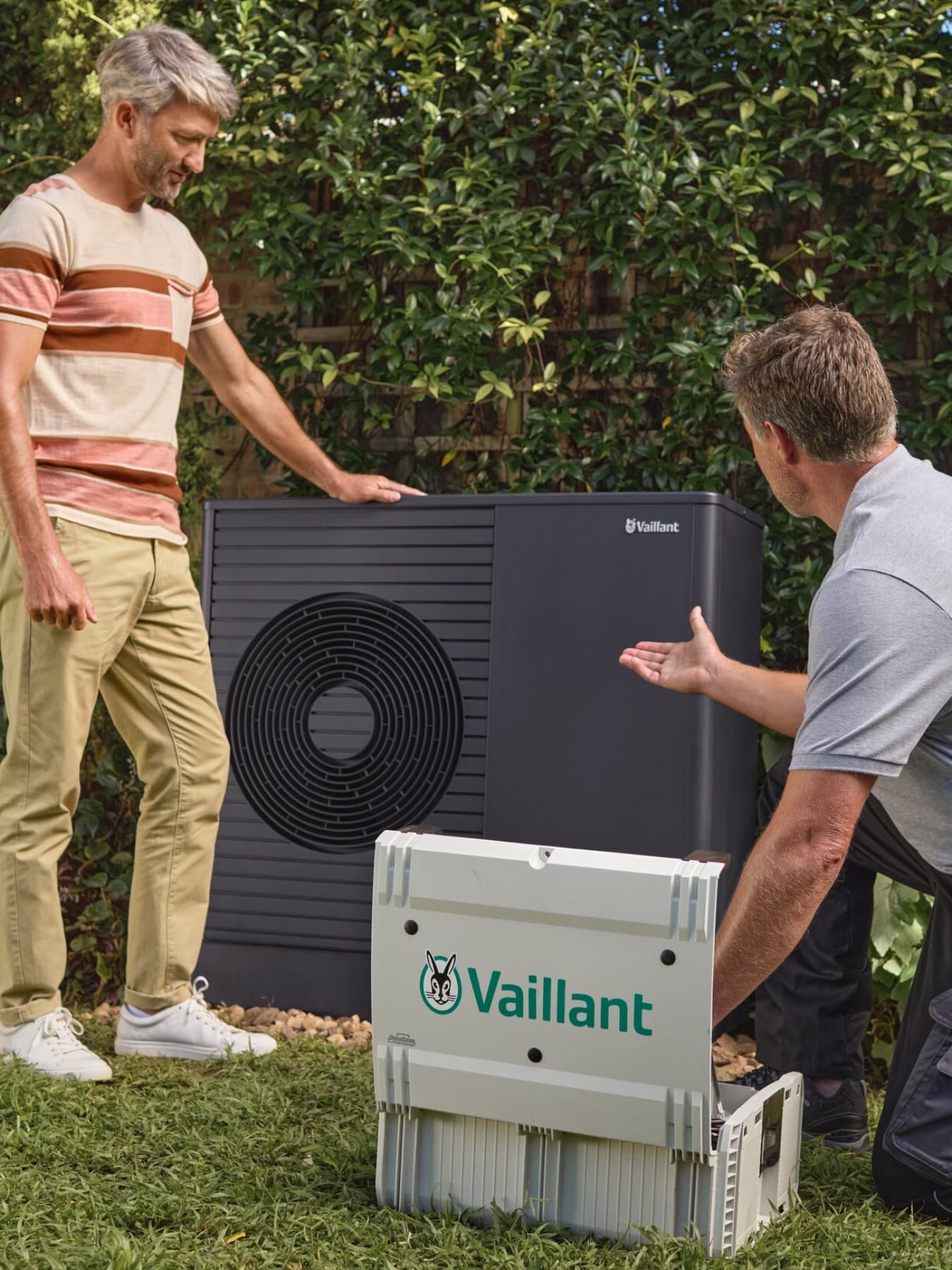 Luft-Wasser-Wärmepumpe aroTHERM plus von Vaillant steht im Garten. Davor steht der Eigentümer und ein Vaillant Fachpartner.
