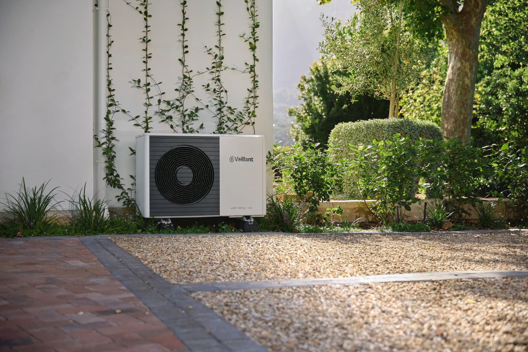 Eine Vaillant Wärmepumpe auf einem Kiesbett, im Hintergrund ist ein digitales grünes V zu sehen.