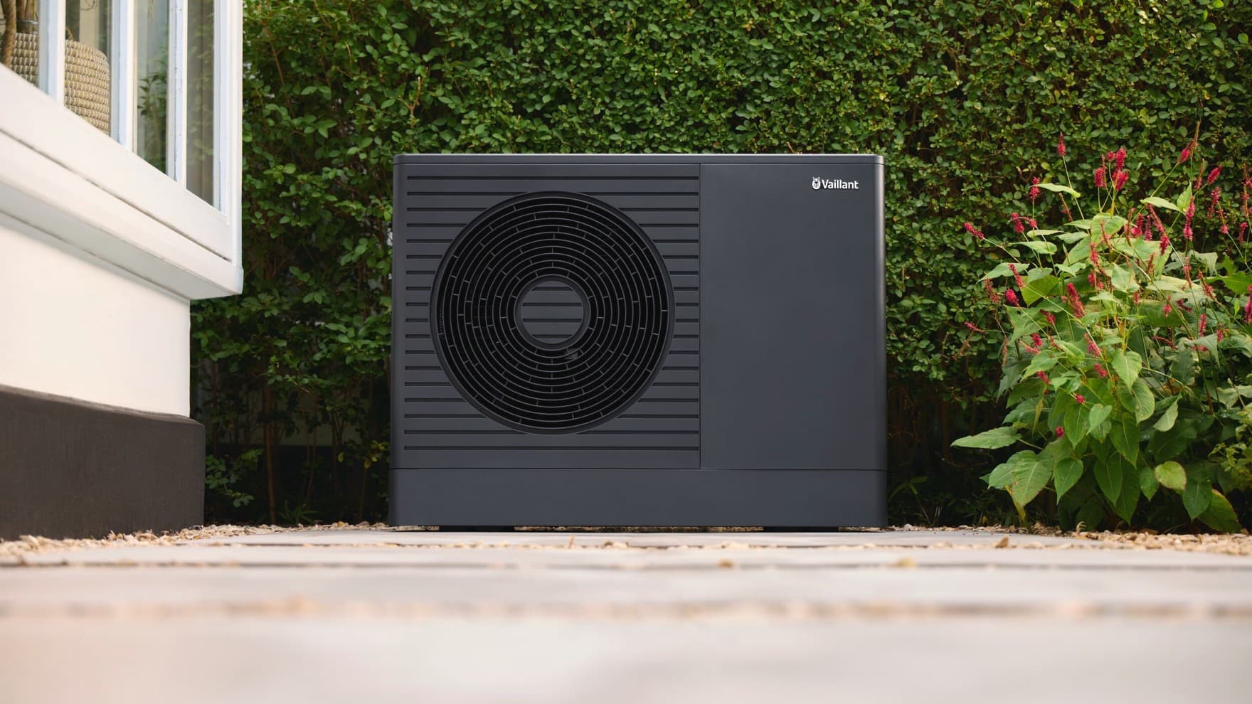 Vaillant Wärmepumpe aroTHERM pro vor einer grünen Hecke neben einem weißen Haus