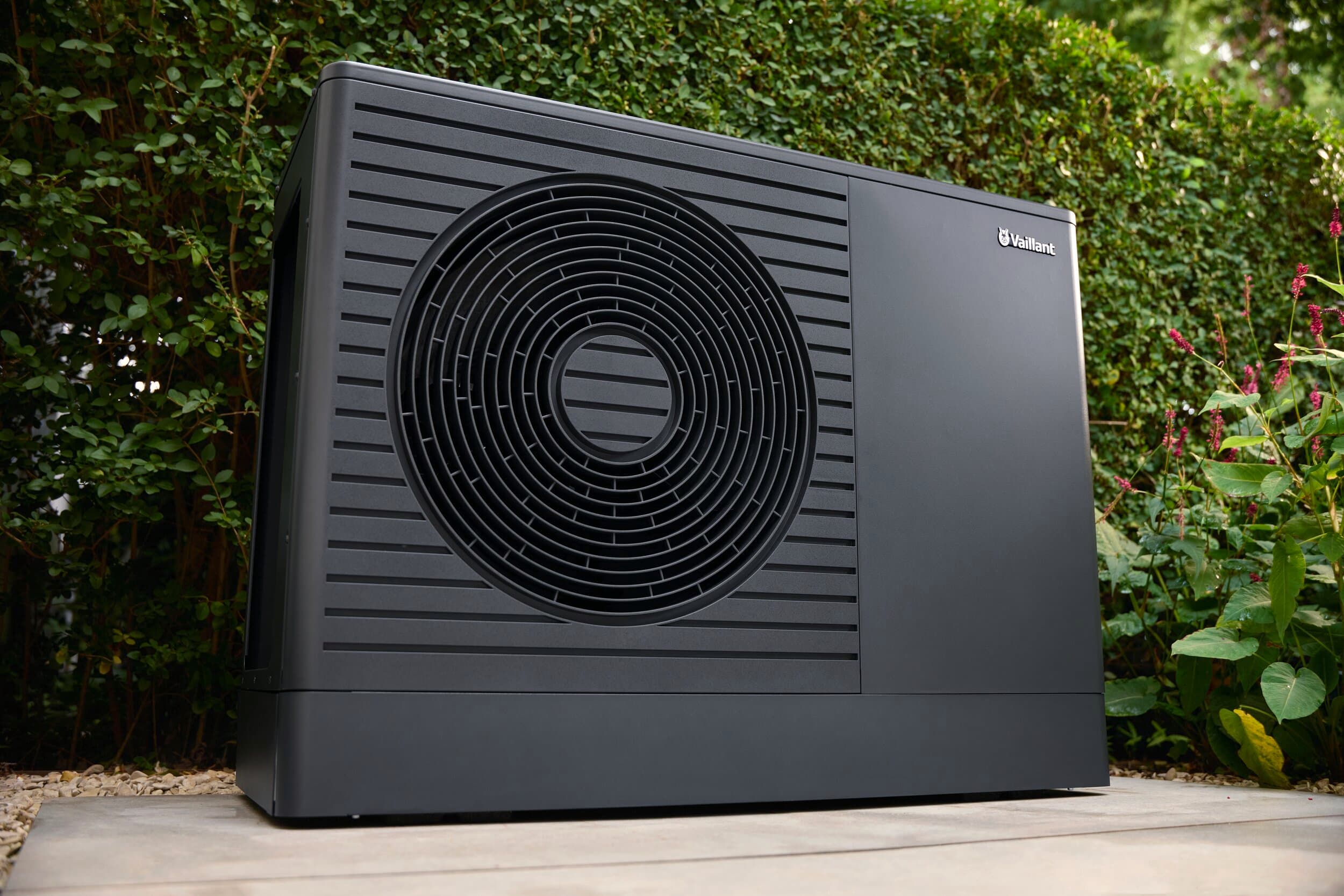 Die neue Vaillant Wärmepumpe aroTHERM pro in Nahaufnahme von unten, sie steht vor einer grünen Hecke.