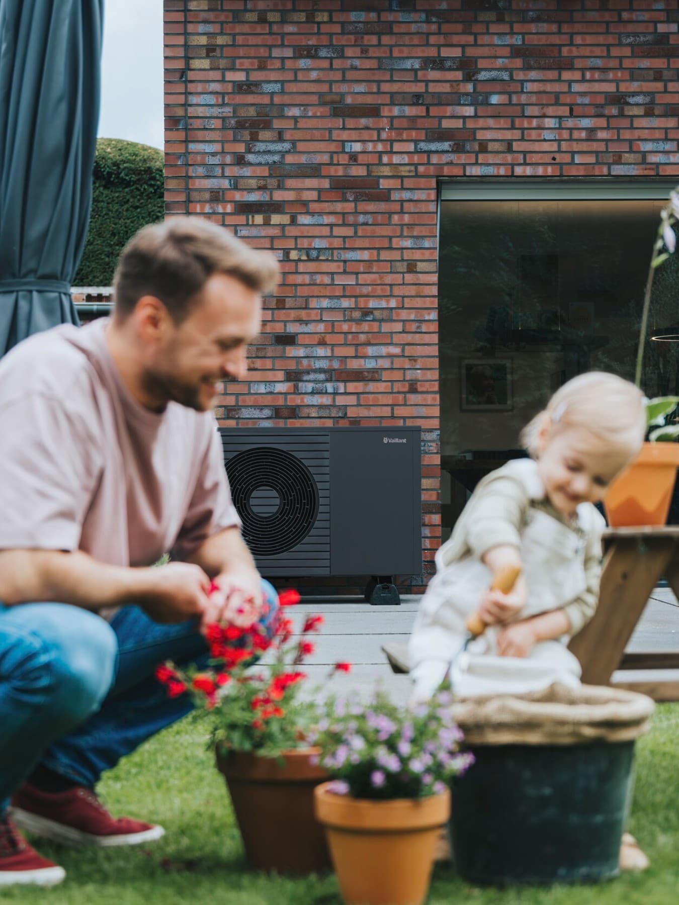 Ein Mann und ein Kind spielen im Garten. Im Hintergrund steht eine neue Vaillant Wärmepumpe vor einem Backsteinhaus.