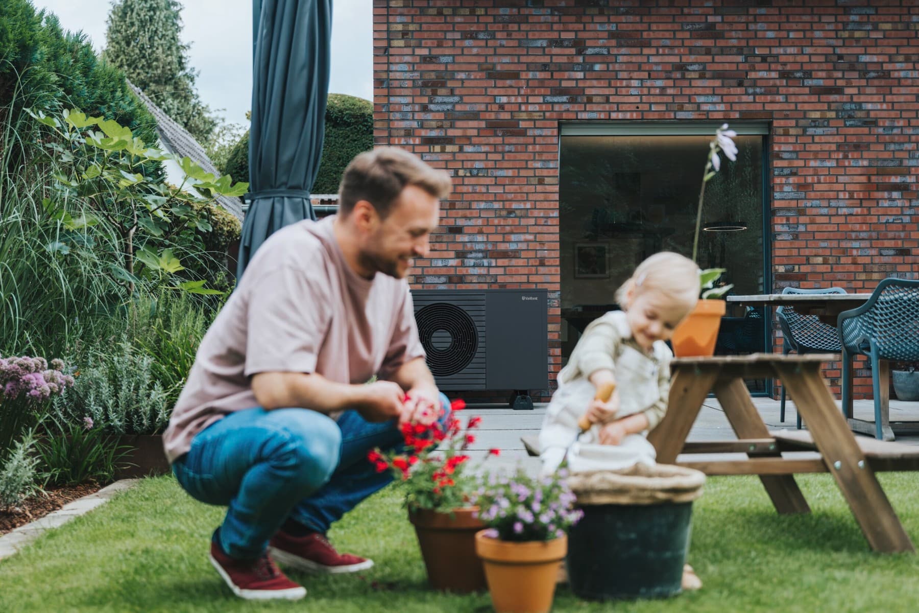 Ein Mann und ein Kind spielen im Garten. Im Hintergrund steht eine neue Vaillant Wärmepumpe vor einem Backsteinhaus.
