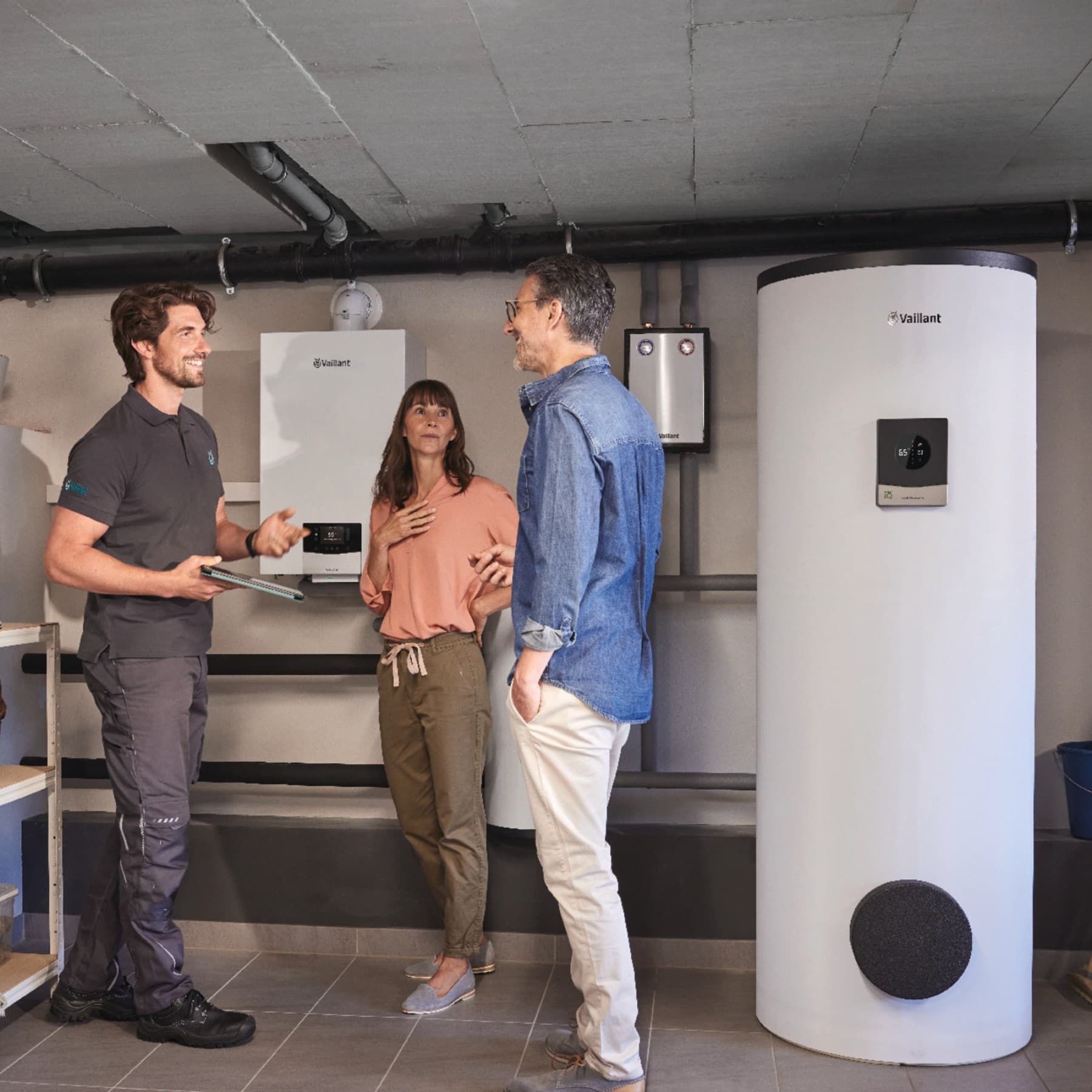 Ehepaar steht mit Vaillant Werkskundendienst-Techniker im Keller vor der neuen Hybridheizung