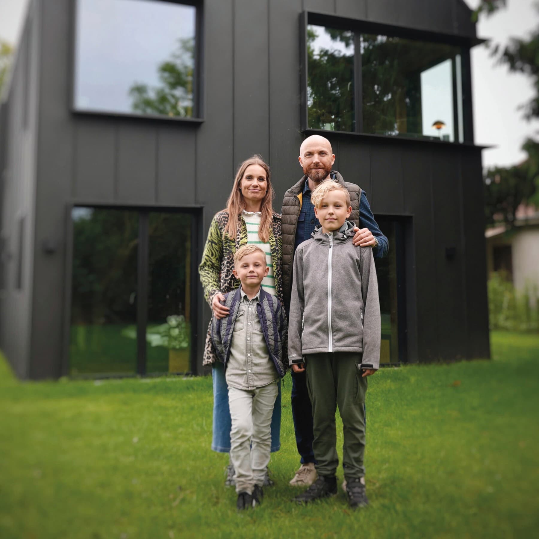 Eine Familie mit zwei Kindern steht vor ihrem Haus im Garten.