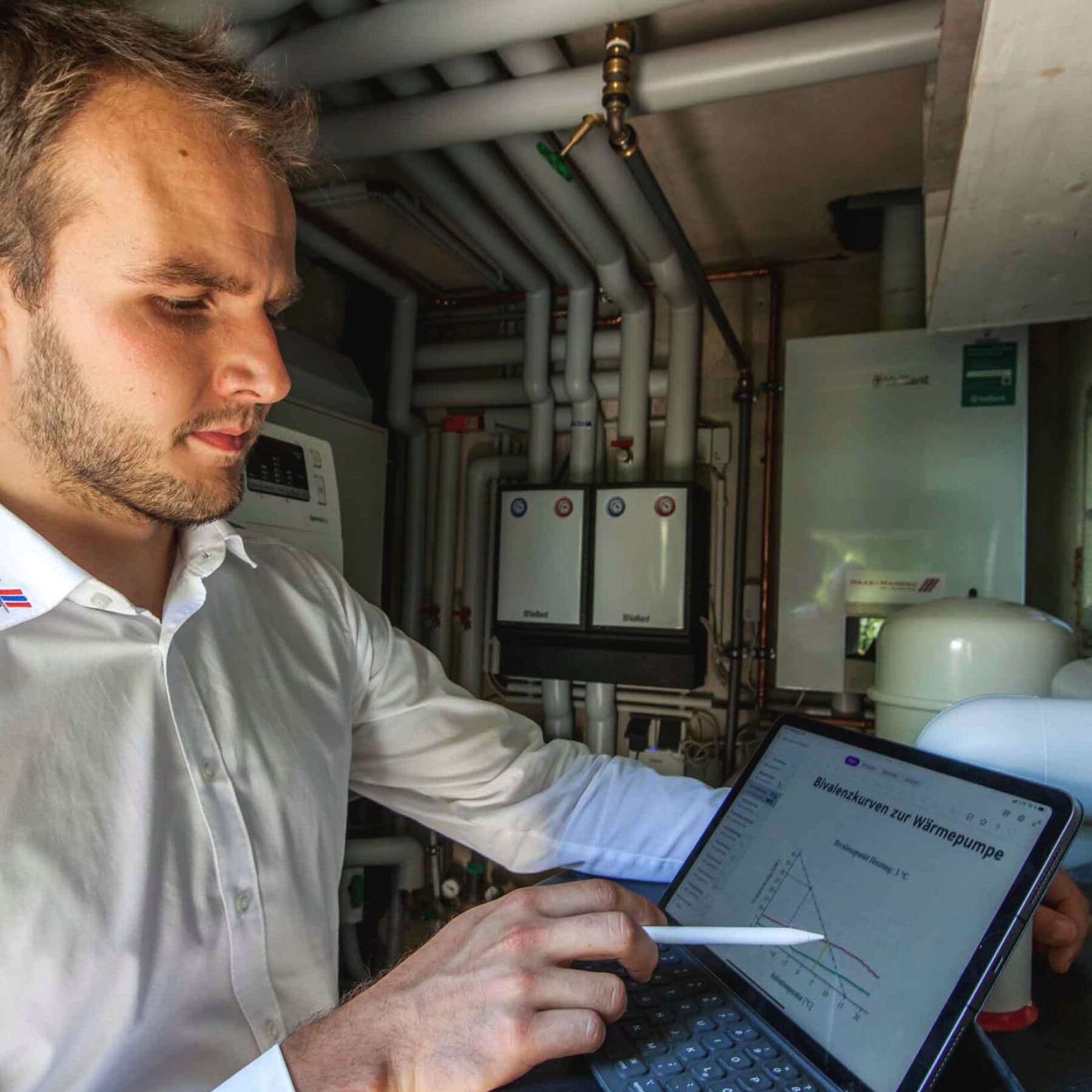 Heizungsbauer steht mit einem Tablet in der linken Hand im Technikraum
