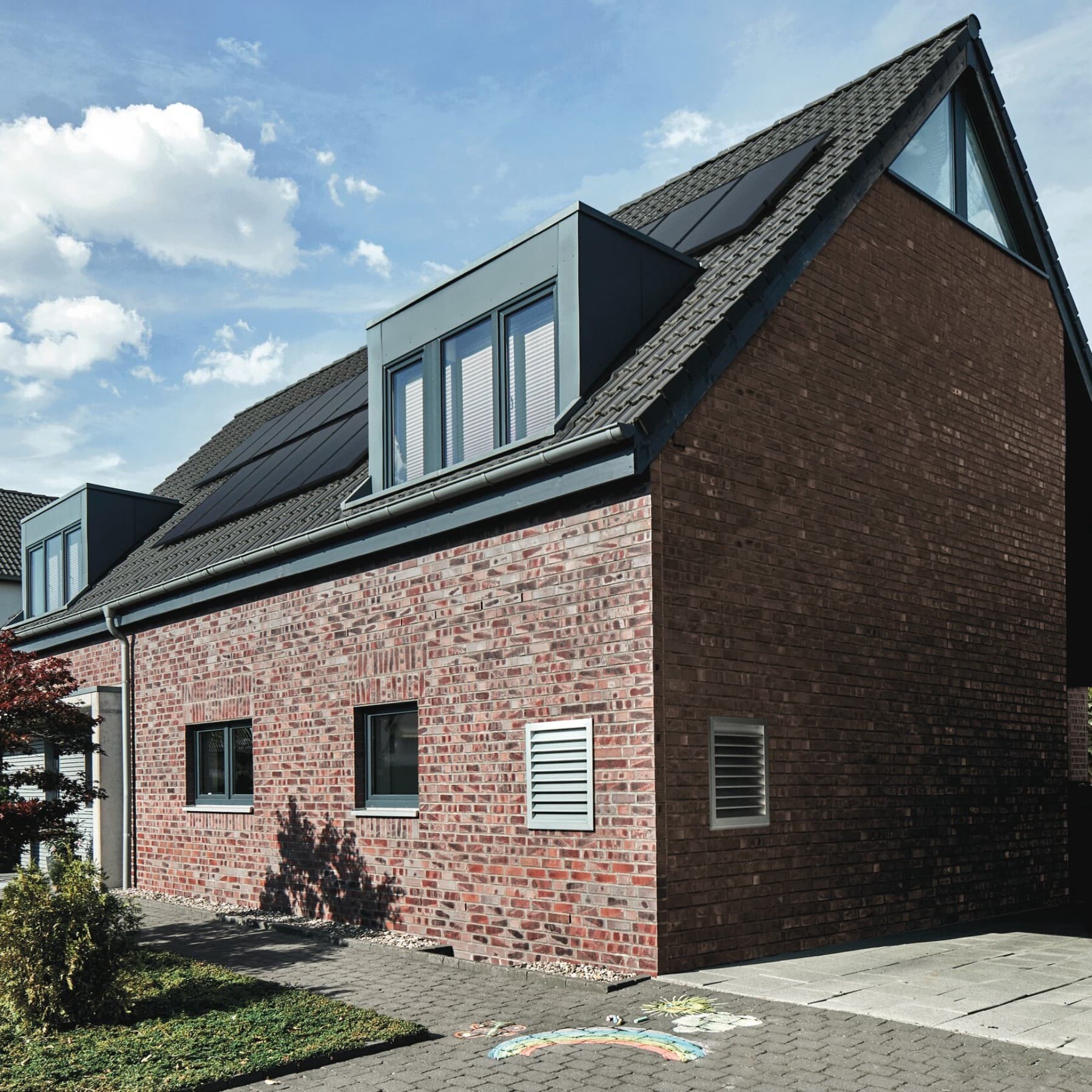 Außenansicht eines Hauses mit Photovoltaik auf dem Dach und Lüftungsgittern in der Hauswand