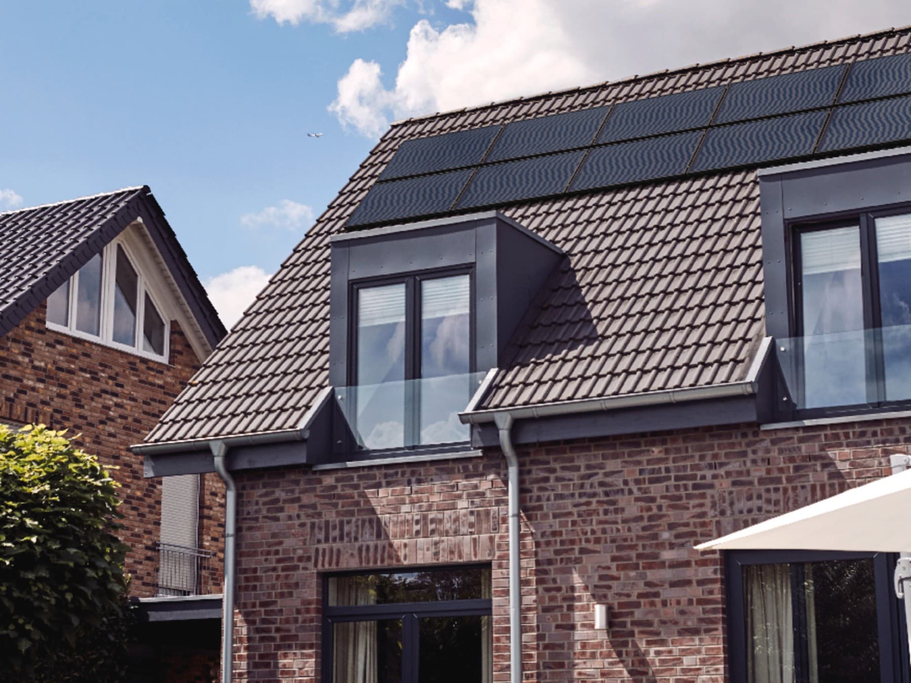 Ein Backsteinhaus mit Baum im Vorgarten und einer PV-Anlage auf dem Dach.