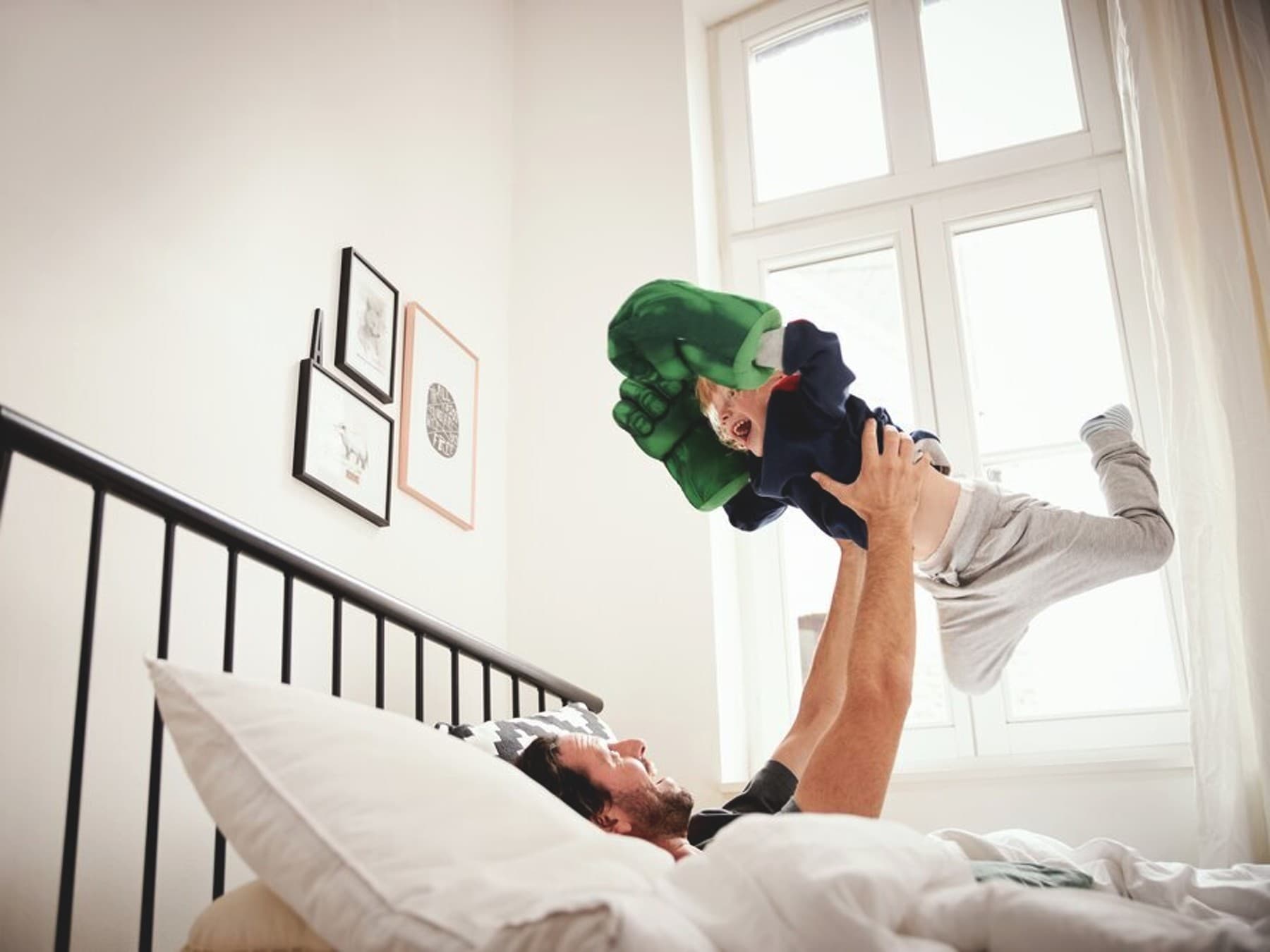 Vater liegt im Bett und hält seinen kleinen Sohn in die Luft.