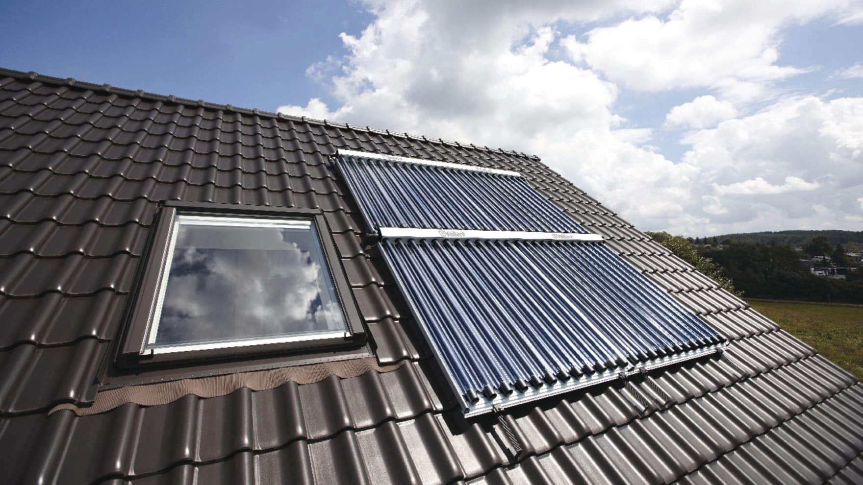 Ein Solarkollektor auf einem Hausdach neben einem Dachfenster.